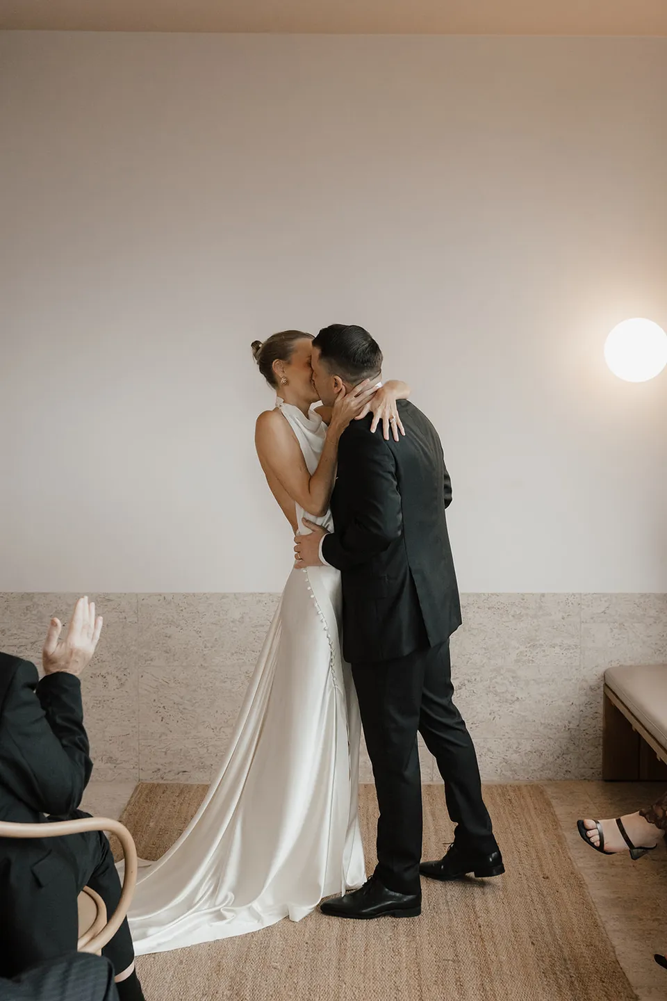 Clare and Matt kissing as their guests applaud in the suite, at The Calile Hotel in Fortitude Valley, Brisbane, for an Elopement Collective elopement. Photo by Harley from Bulb Creative.