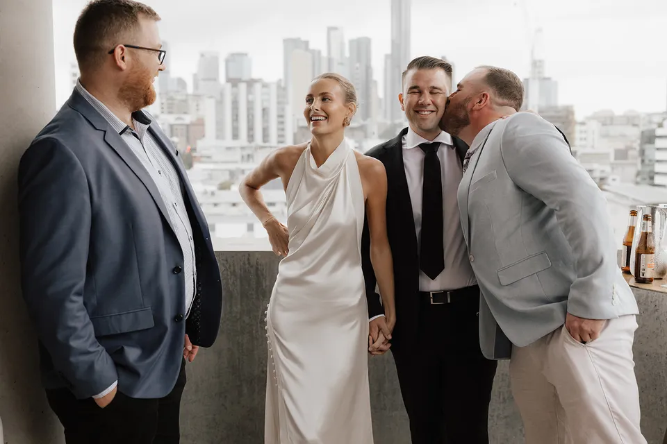 Clare and Matt smiling with guests on the hotel terrace after their ceremony, at The Calile Hotel in Fortitude Valley, Brisbane, for an Elopement Collective elopement. Photo by Harley from Bulb Creative.