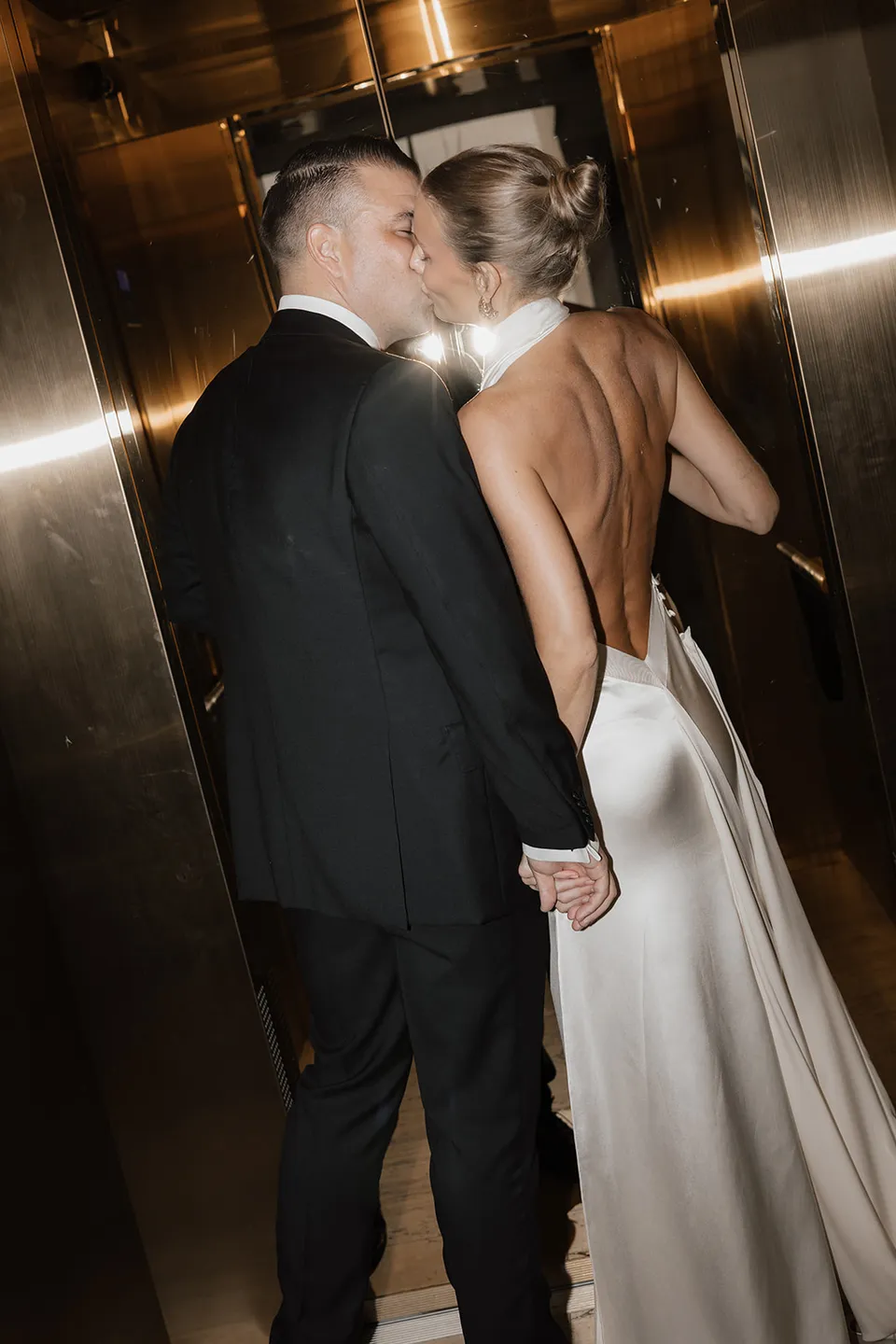 Clare and Matt kissing in the hotel’s gold mirrored lift, at The Calile Hotel in Fortitude Valley, Brisbane, for an Elopement Collective elopement. Photo by Harley from Bulb Creative.