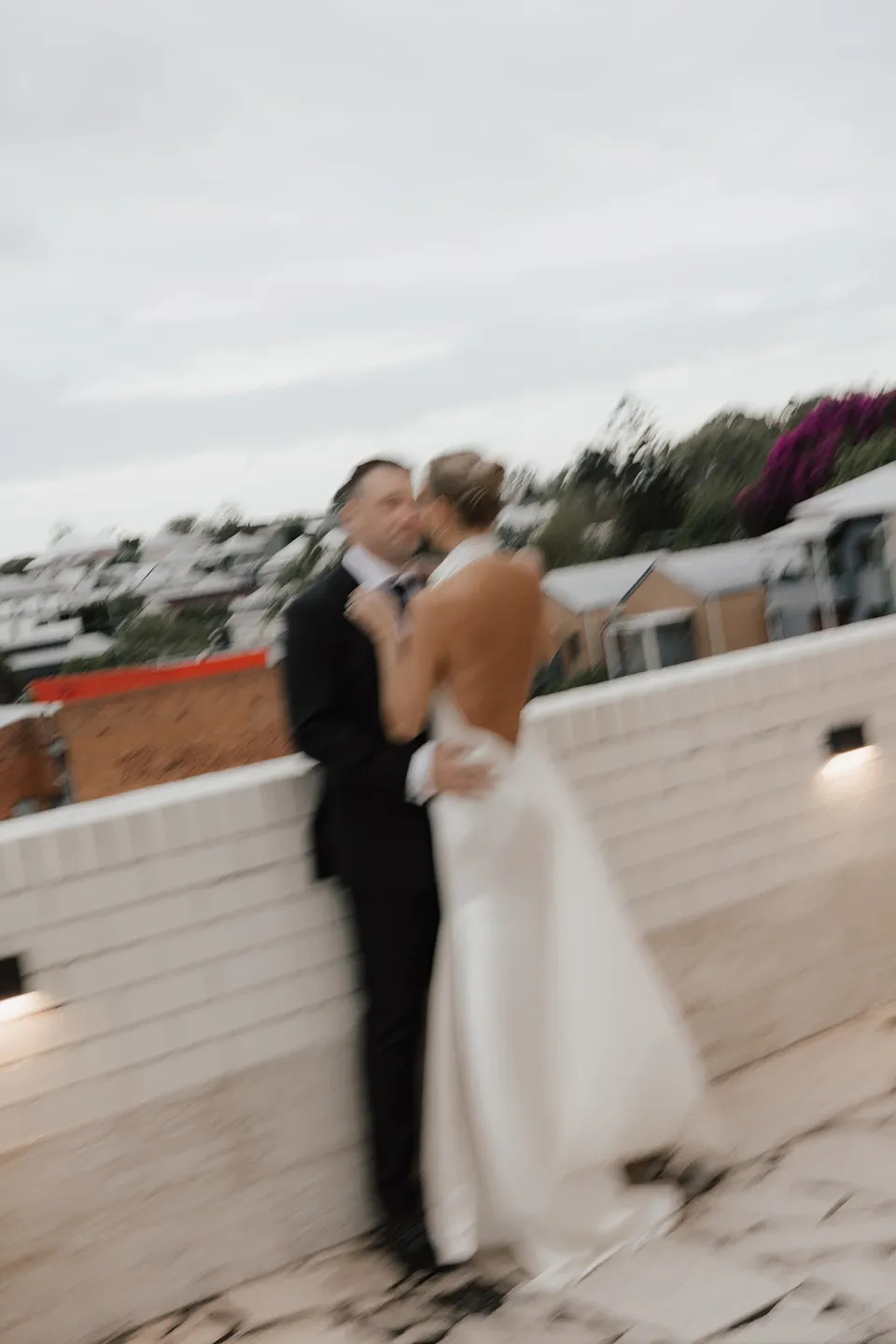 Softly blurred portrait of Clare and Matt embracing on the hotel terrace, at The Calile Hotel in Fortitude Valley, Brisbane, for an Elopement Collective elopement. Photo by Harley from Bulb Creative.