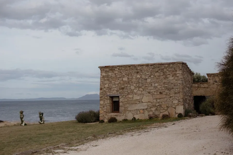 A stone cottage beside the sea beneath a cloudy sky.