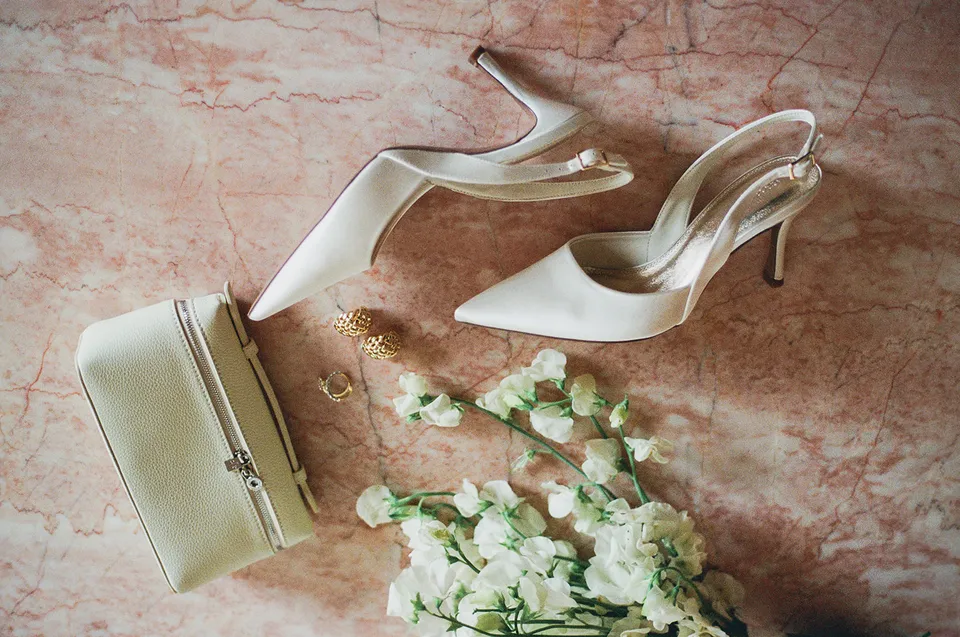 Clare’s ivory ASOS heels, pale Loro Piana bag, gold jewellery and white flowers by Mrs Gibbons on pink stone, at The Calile Hotel in Fortitude Valley, Brisbane, for an Elopement Collective elopement. Photo by Harley from Bulb Creative.
