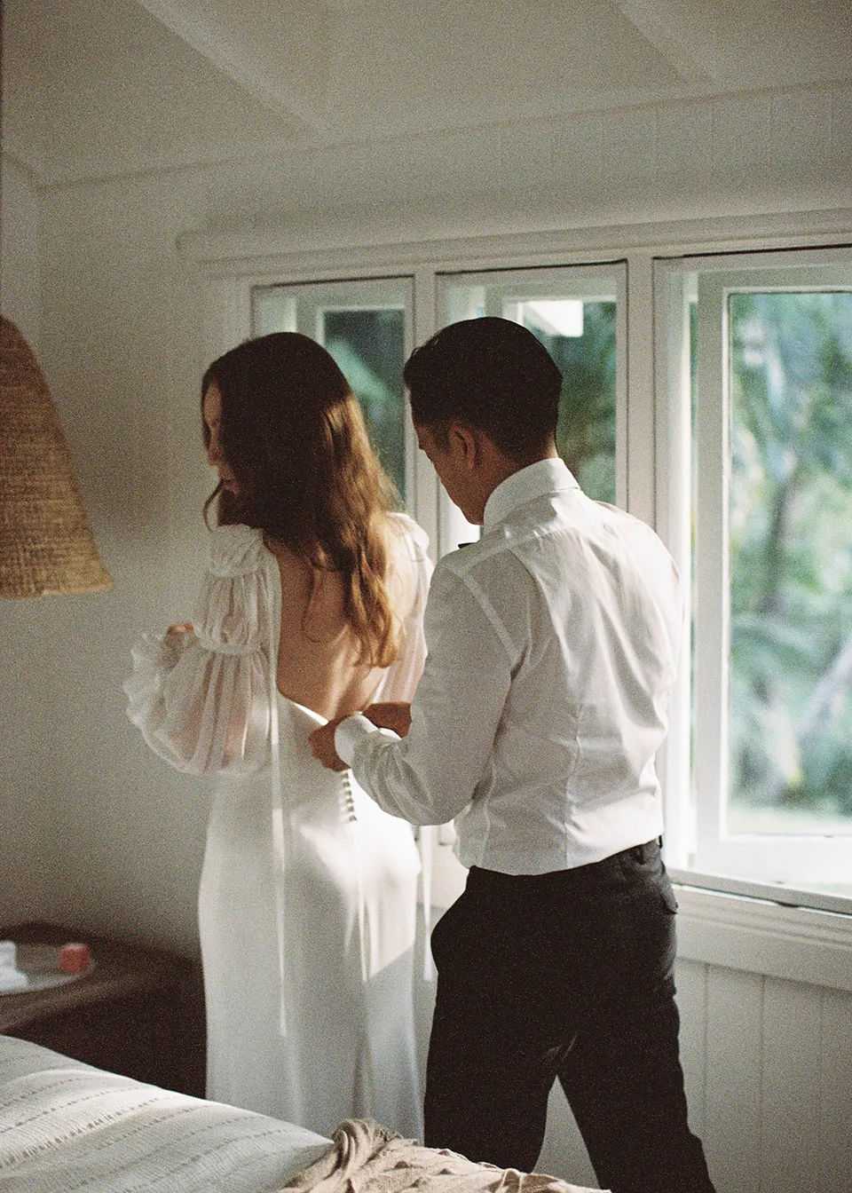 On 35mm film: The couple getting ready together in the soft window light. At Fig Tree Villa in Ewingsdale, Byron Bay, for an Elopement Collective elopement. Photograph by Bulb Creative.
