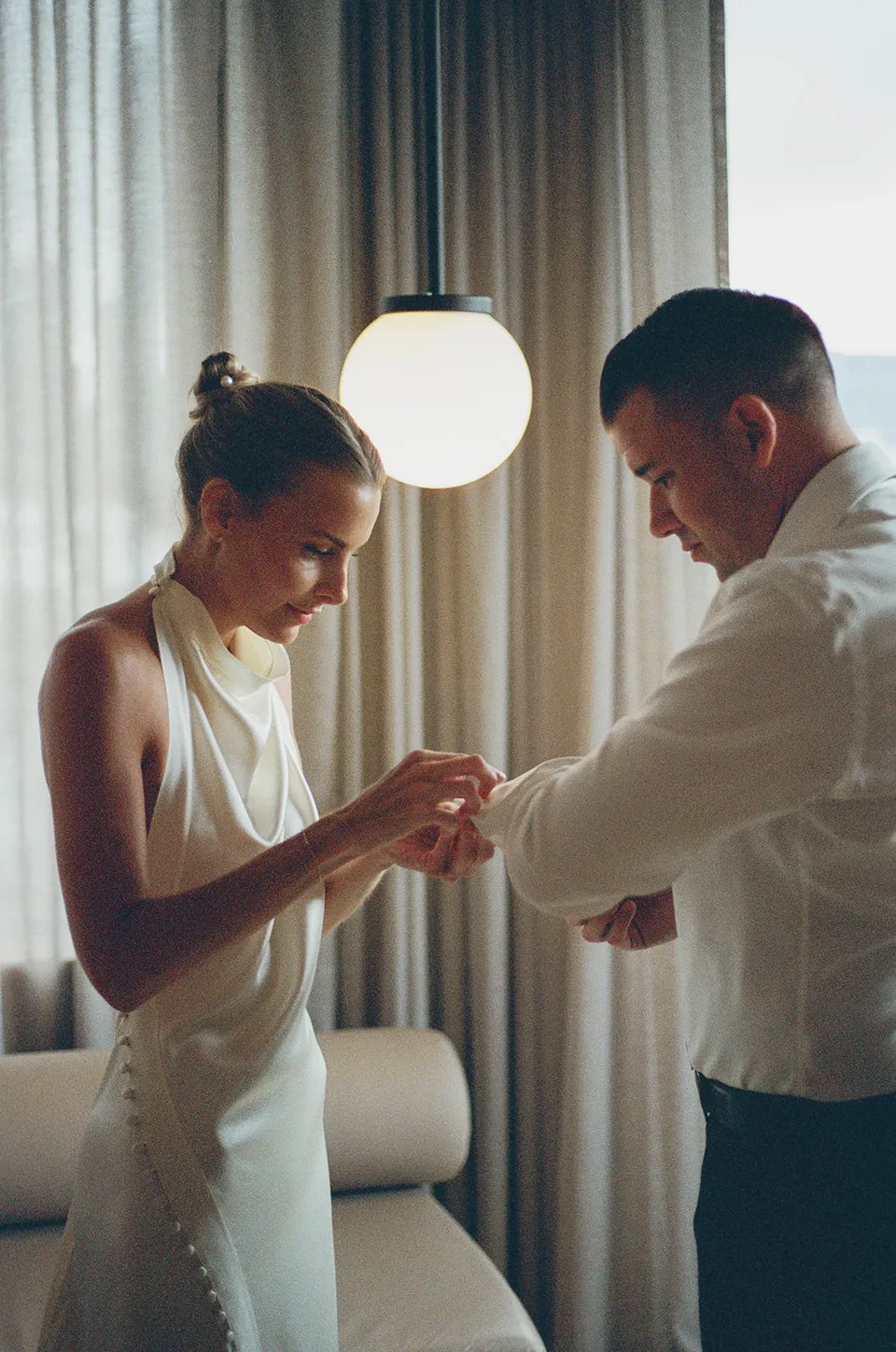 Clare and Matt getting ready together beside a suite window, at The Calile Hotel in Fortitude Valley, Brisbane, for an Elopement Collective elopement. Photo by Harley from Bulb Creative.