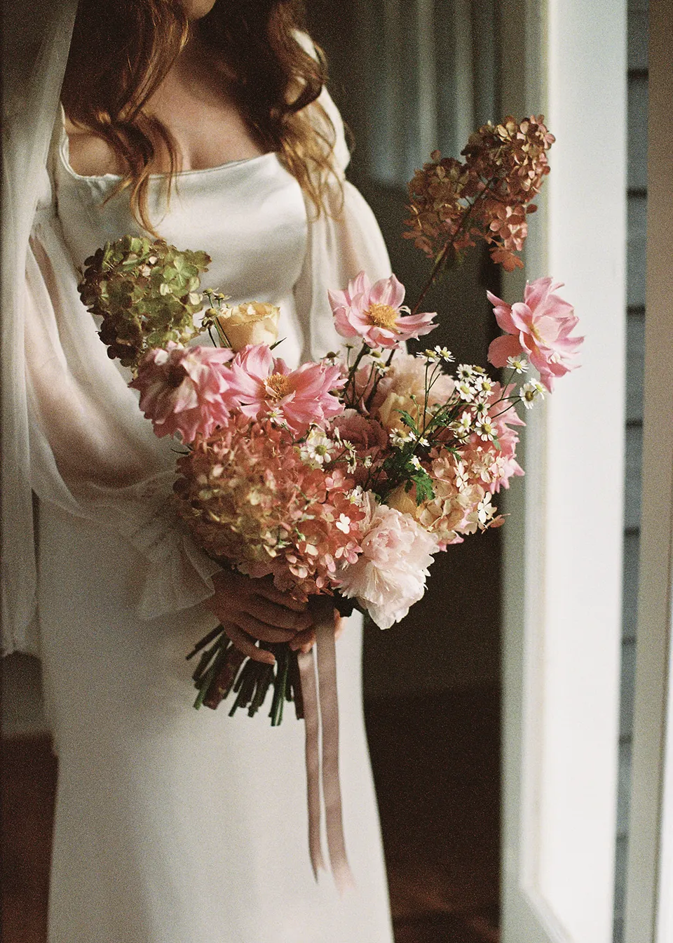 On 35mm film: Elyse holding her pink and cream bouquet in soft indoor light, with flowers by The Perfect Party Co. At Fig Tree Villa in Ewingsdale, Byron Bay, for an Elopement Collective elopement. Photograph by Bulb Creative.
