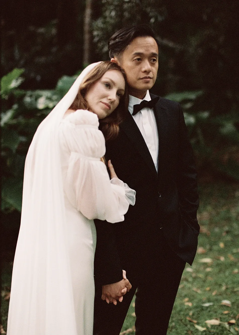 On 35mm film: Elyse resting her head on Jonathan's shoulder while they hold hands. At Fig Tree Villa in Ewingsdale, Byron Bay, for an Elopement Collective elopement. Photograph by Bulb Creative.