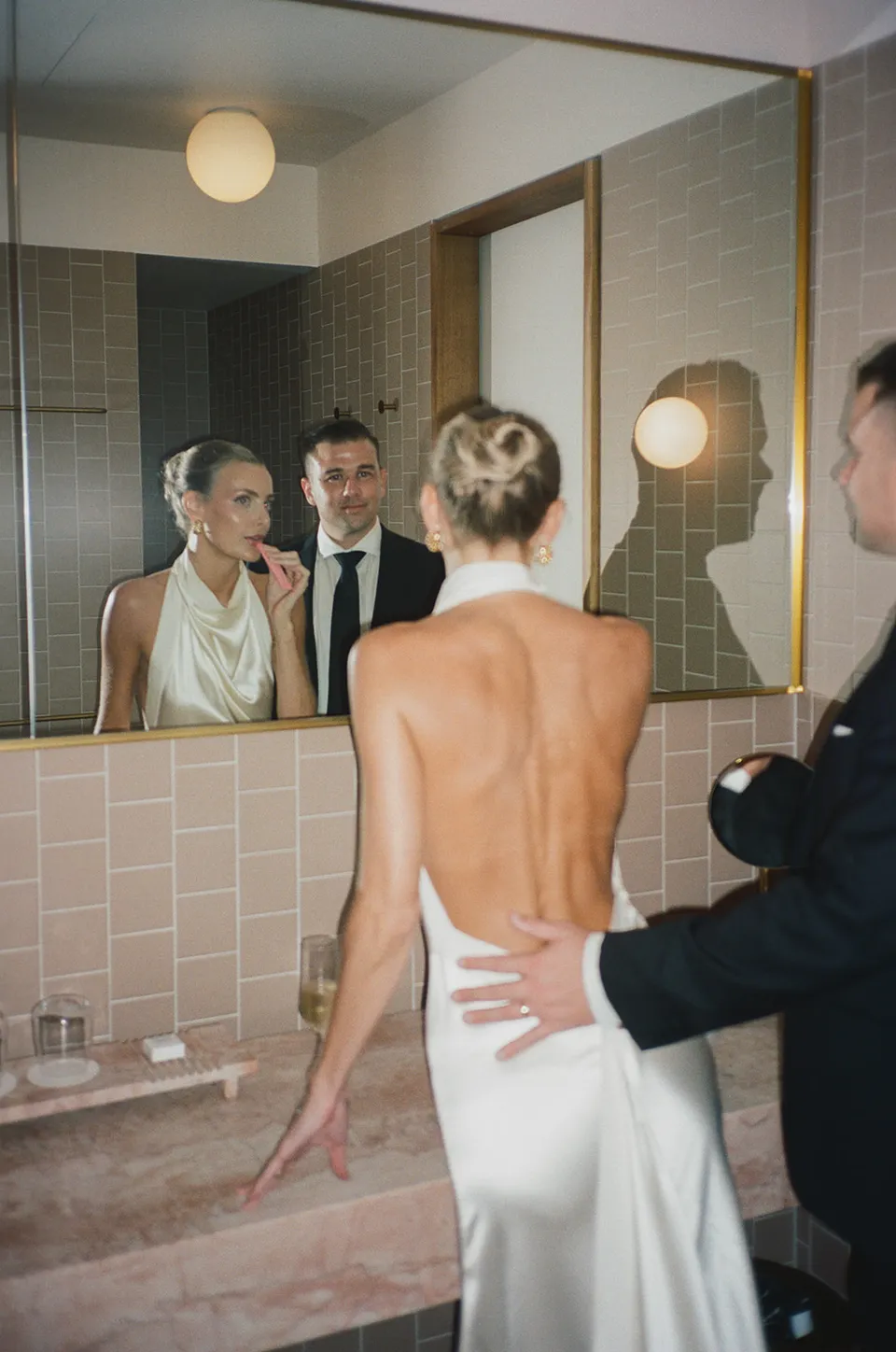Clare and Matt reflected in their suite’s bathroom mirror, at The Calile Hotel in Fortitude Valley, Brisbane, for an Elopement Collective elopement. Photo by Harley from Bulb Creative.