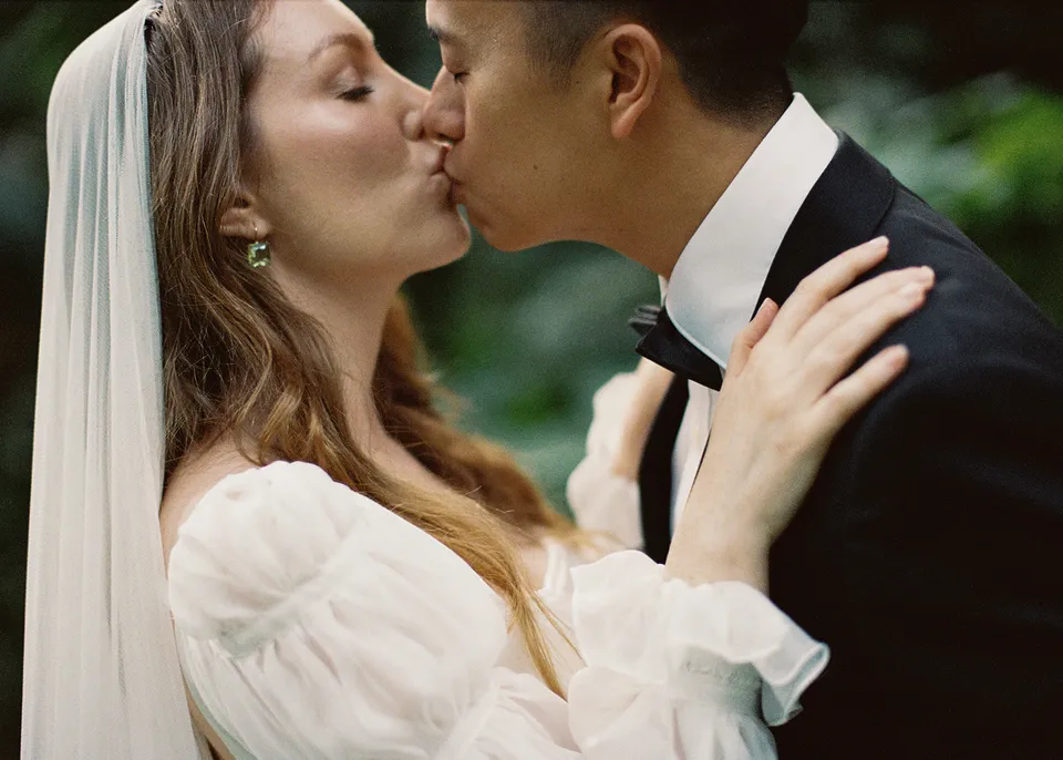 On 35mm film: Elyse and Jonathan kissing with her hand resting on his shoulder. At Fig Tree Villa in Ewingsdale, Byron Bay, for an Elopement Collective elopement. Photograph by Bulb Creative.