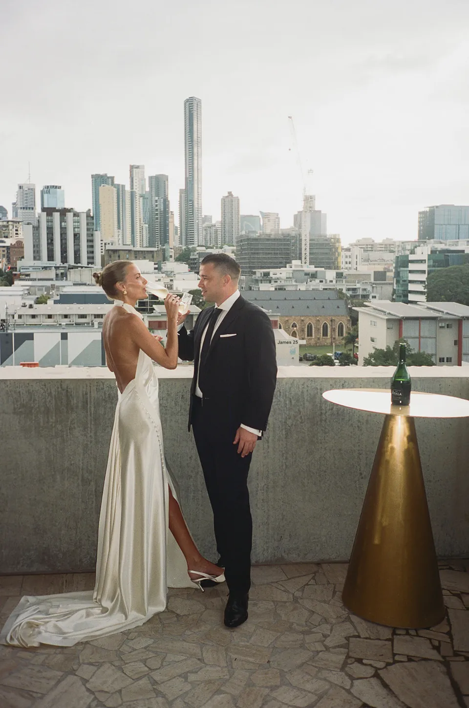 Clare and Matt facing each other on a terrace overlooking the city, at The Calile Hotel in Fortitude Valley, Brisbane, for an Elopement Collective elopement. Photo by Harley from Bulb Creative.