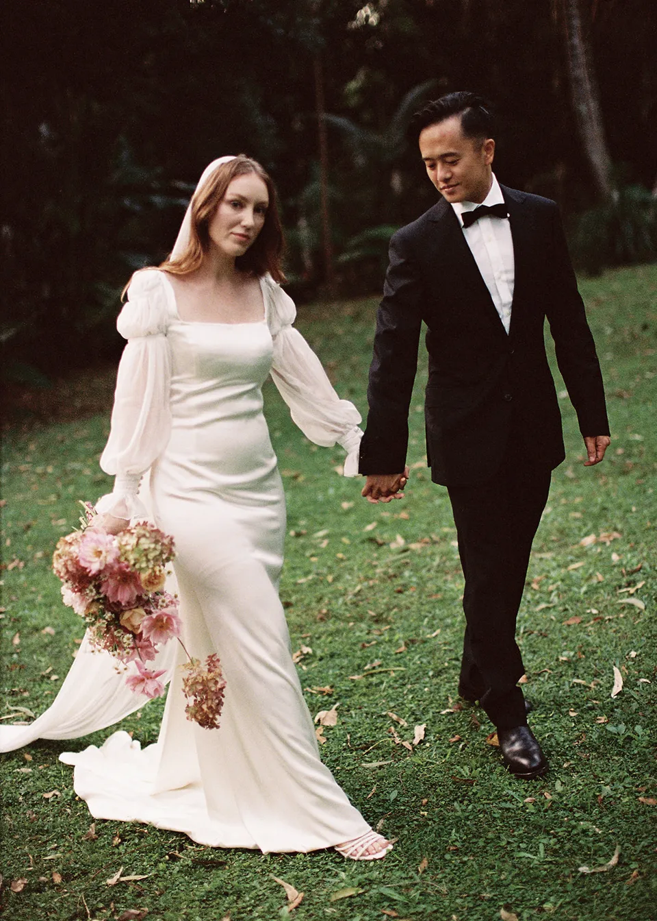 On 35mm film: The couple smiling together while walking across the grass. At Fig Tree Villa in Ewingsdale, Byron Bay, for an Elopement Collective elopement. Photograph by Bulb Creative.