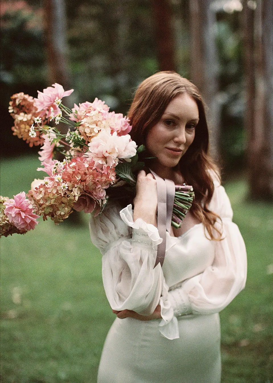 On 35mm film: Elyse resting her pink bouquet against her shoulder, with flowers by The Perfect Party Co. At Fig Tree Villa in Ewingsdale, Byron Bay, for an Elopement Collective elopement. Photograph by Bulb Creative.