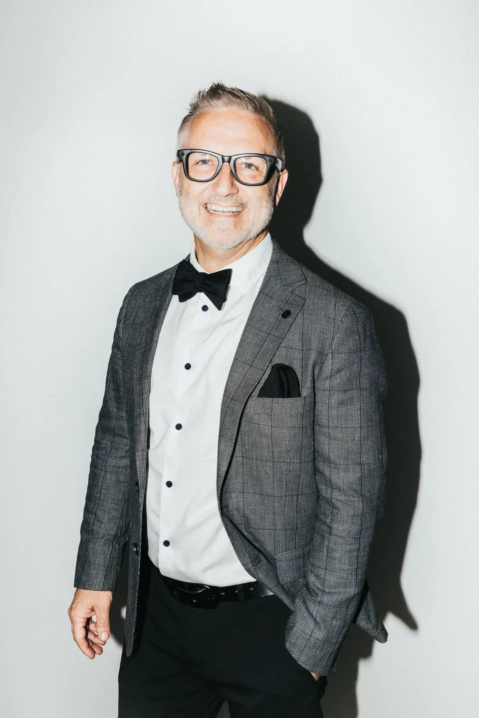 Jake Smith smiling in glasses, a grey suit and black bow tie