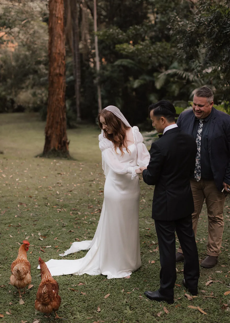 Elyse and Jonathan watching the hens wandering through their ceremony. At Fig Tree Villa in Ewingsdale, Byron Bay, for an Elopement Collective elopement. Photograph by Bulb Creative.