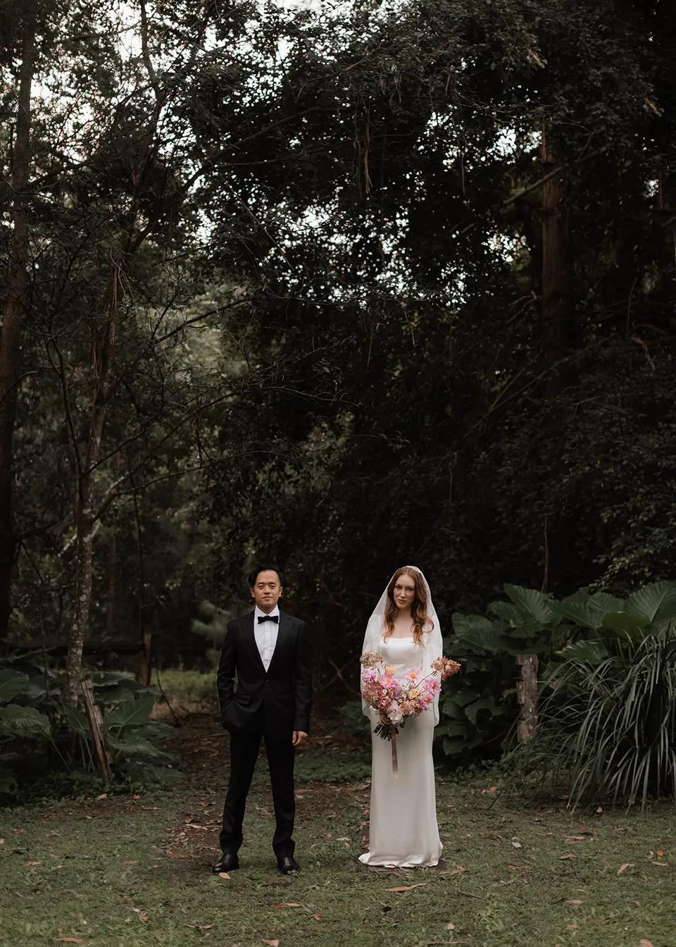 Wide portrait of Elyse and Jonathan together beneath the garden canopy. At Fig Tree Villa in Ewingsdale, Byron Bay, for an Elopement Collective elopement. Photograph by Bulb Creative.