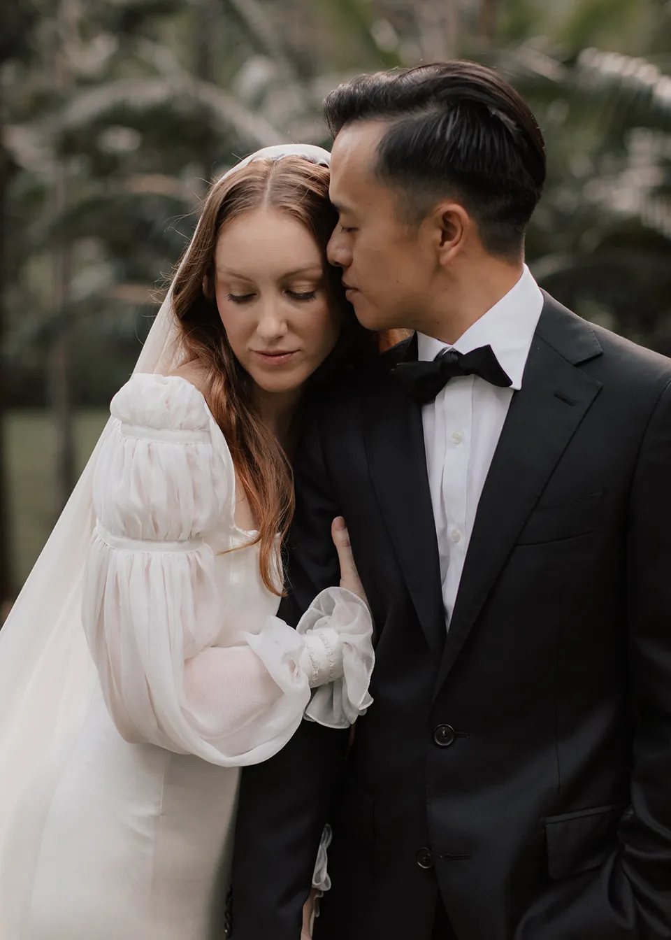 Jonathan kissing Elyse's forehead as she leans against him. At Fig Tree Villa in Ewingsdale, Byron Bay, for an Elopement Collective elopement. Photograph by Bulb Creative.