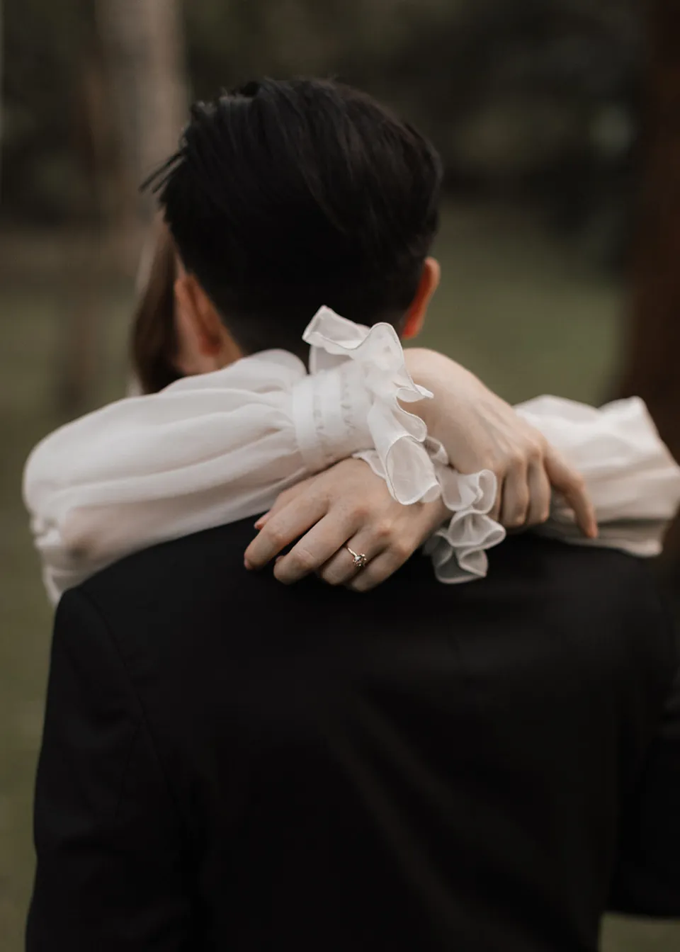 Close-up of Elyse's hands around Jonathan's shoulders. At Fig Tree Villa in Ewingsdale, Byron Bay, for an Elopement Collective elopement. Photograph by Bulb Creative.
