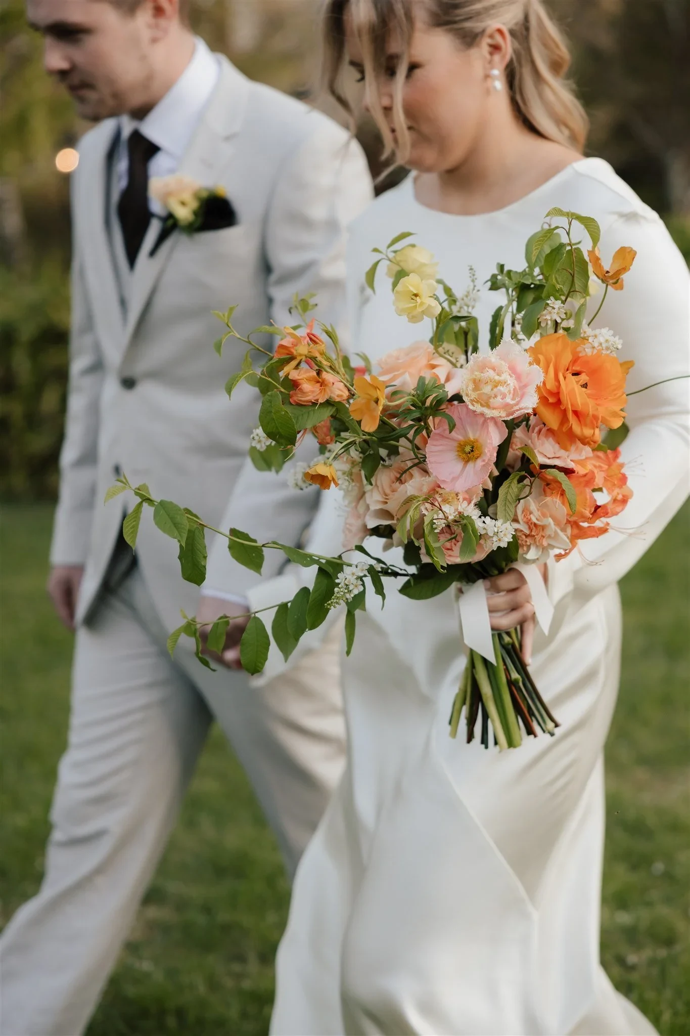 Close portrait of Maddy carrying her orange and pink bouquet by The Flower Jar beside Cameron, at The Mayor’s Residence in Daylesford, Victoria, for an Elopement Collective elopement. Photo by Bulb Creative.