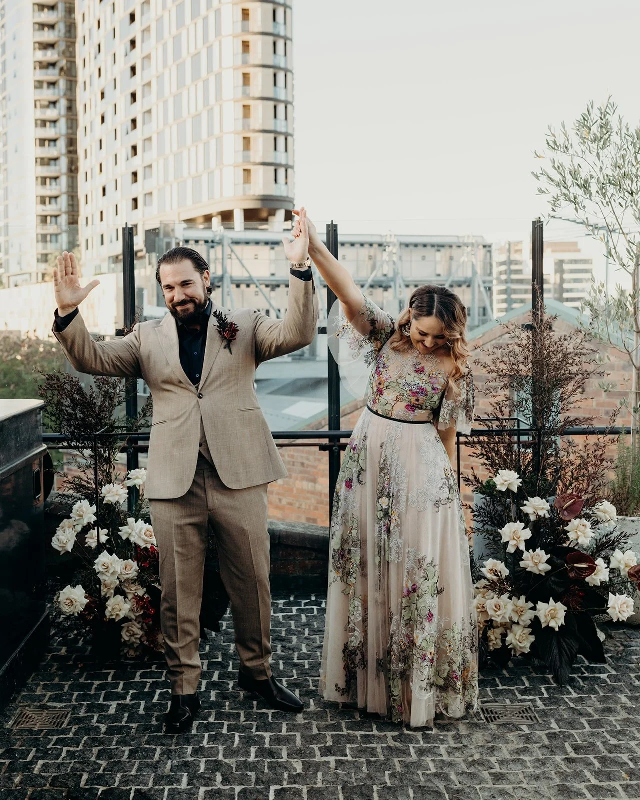 Victoria and Daniel raising their joined hands in celebration after their rooftop ceremony, at Agnes Restaurant in Fortitude Valley, Brisbane, for an Elopement Collective elopement. Photo by Tessa Shannon.