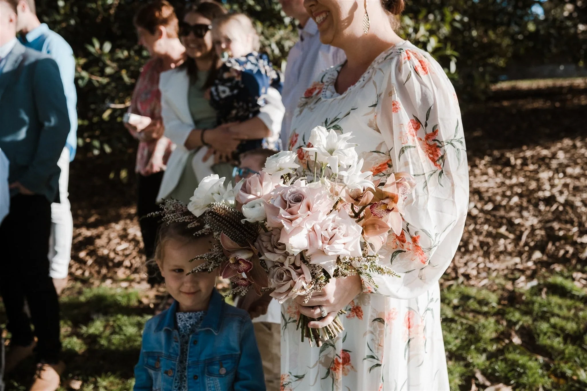 A guest holding Alyce’s pink and white bouquet by The Lillipillian beside a child among the ceremony guests, at Observatory Hill in Sydney, New South Wales, for an Elopement Collective elopement. Photo by Jason Corroto.