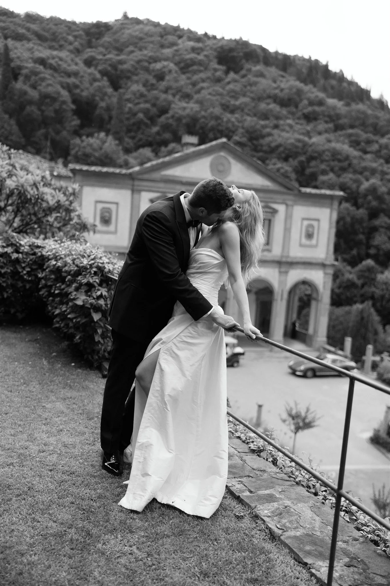Black-and-white photograph of Holly and Matt kissing along the garden path in front of the villa, at Belmond Villa San Michele in Fiesole, overlooking Florence, Tuscany, Italy, for an Elopement Collective elopement. Photo by Khara from House of Lucie.