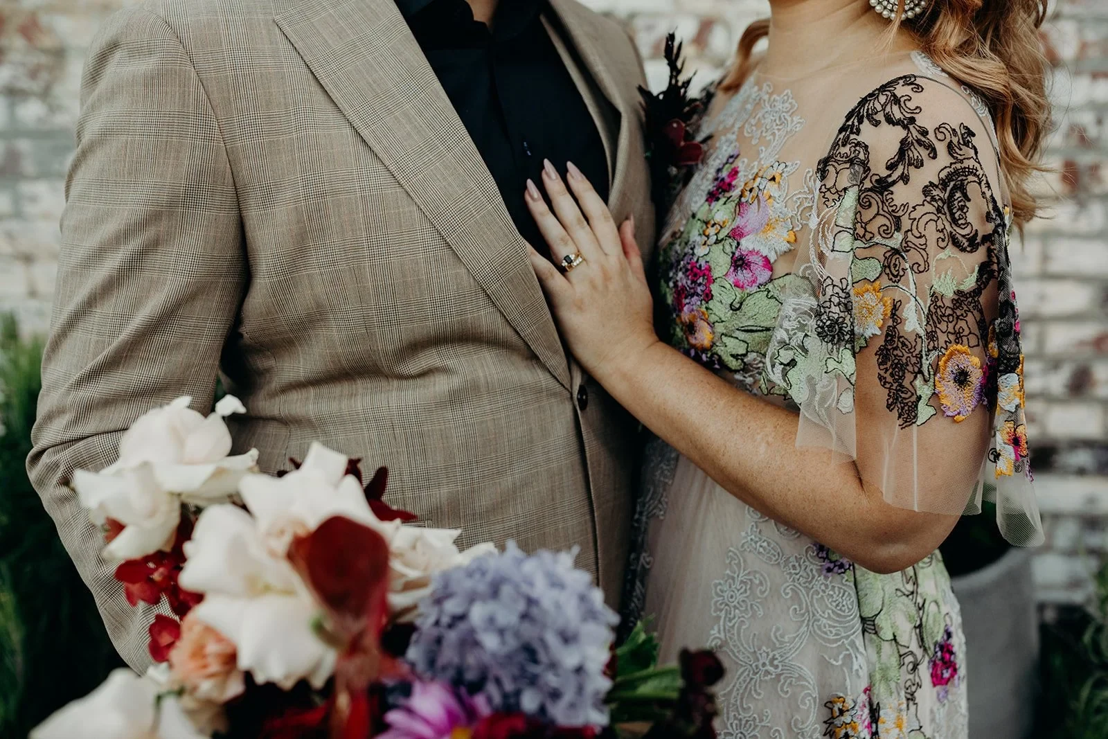 Detail of Victoria’s hand on Daniel’s beige suit, with her floral dress and bouquet by Mrs Gibbons Flowers, in Fortitude Valley, Brisbane, for an Elopement Collective elopement. Photo by Tessa Shannon.