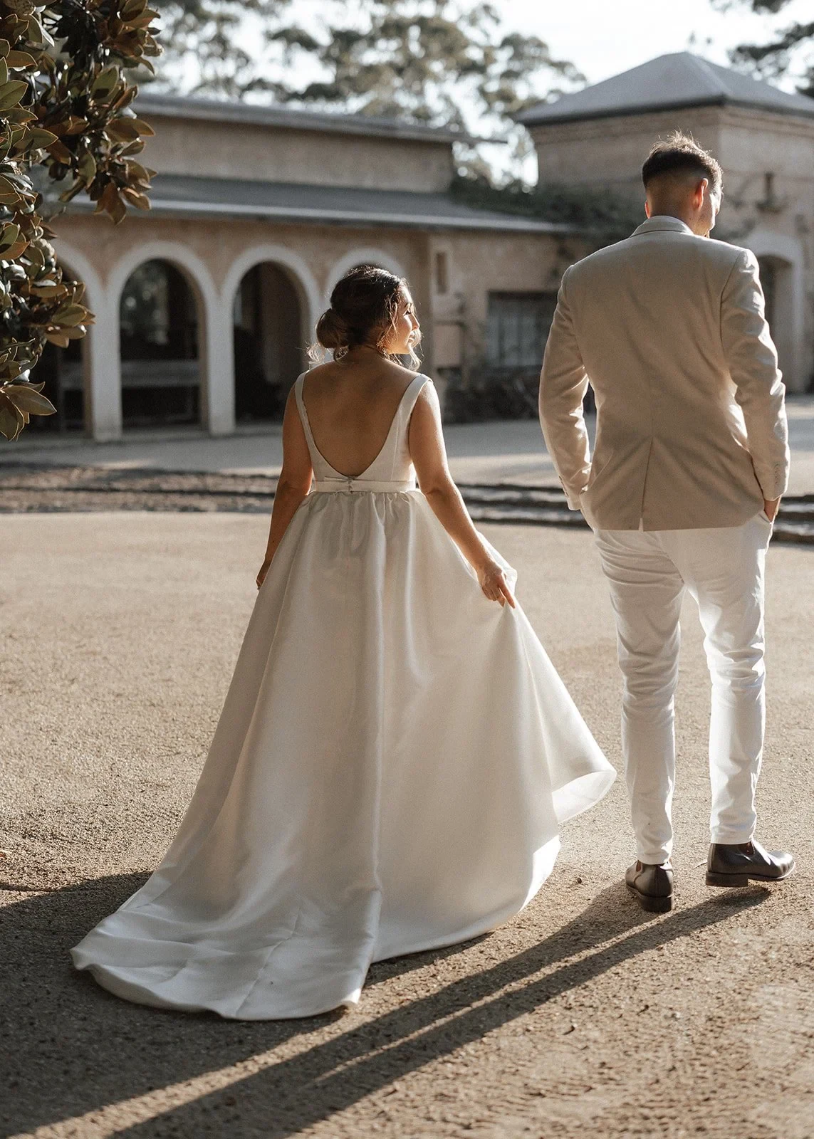 A couple holding hands as they walk towards an arched stone building in afternoon light, during an elopement created by The Elopement Collective.