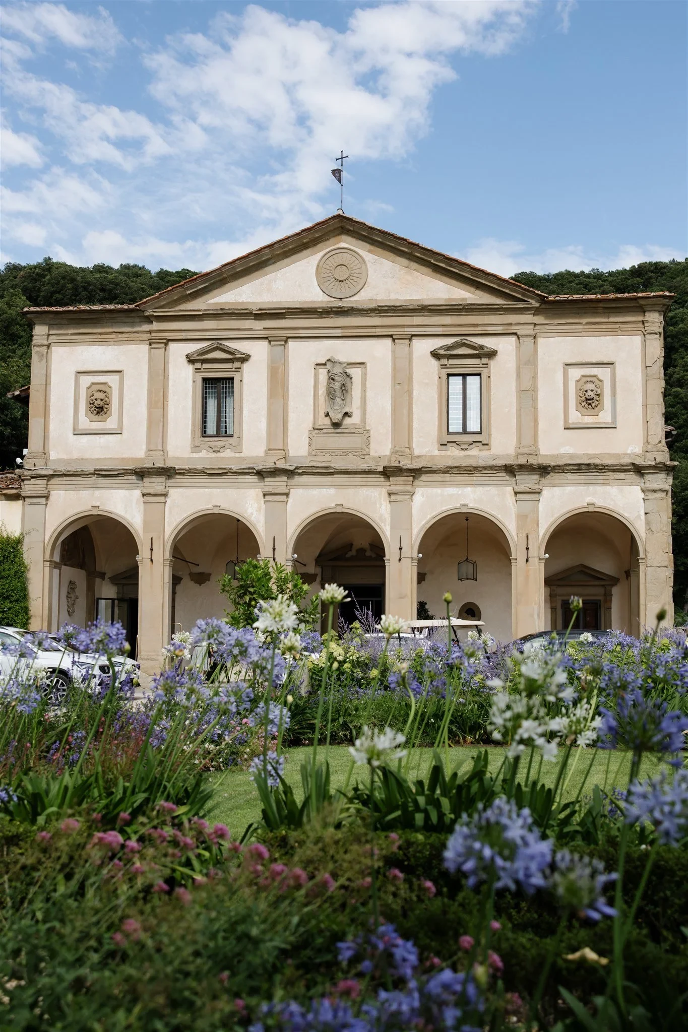 The villa’s ornate stone façade and arched loggia above a garden of purple flowers, at Belmond Villa San Michele in Fiesole, overlooking Florence, Tuscany, Italy, for an Elopement Collective elopement. Photo by Khara from House of Lucie.