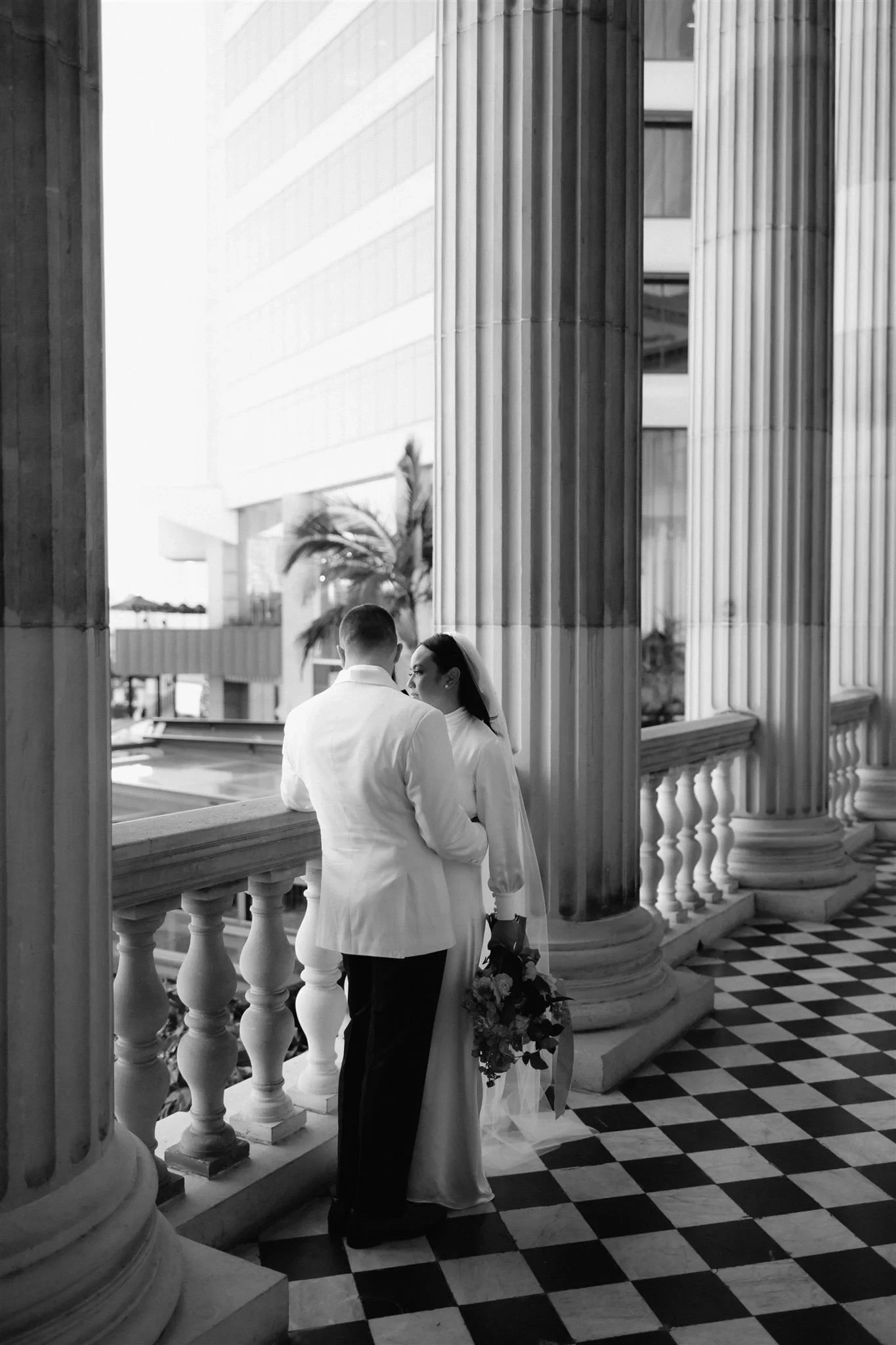 A couple leaning in for a kiss between stone columns above a chequered floor, during an elopement created by The Elopement Collective. Photo by Bulb Creative.