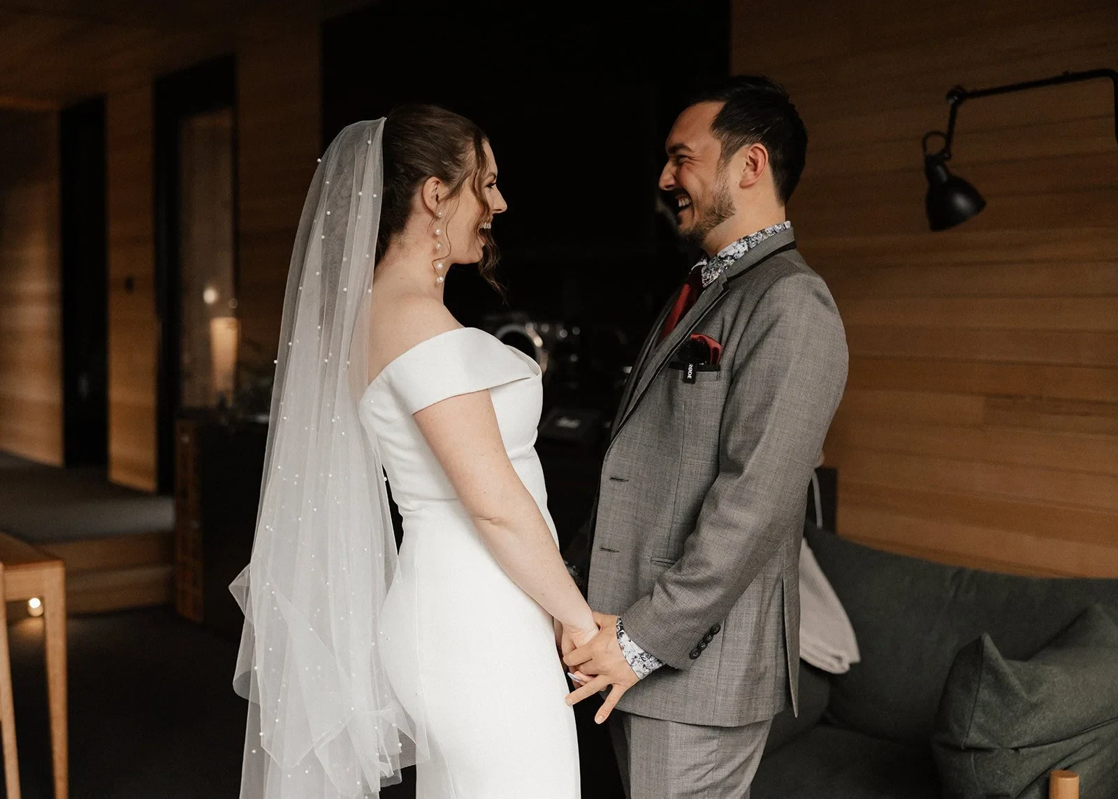 Sarah and Jono smiling at each other and holding hands inside the timber-lined room, at Pumphouse Point, Lake St Clair, Tasmania, for an Elopement Collective elopement. Photo by Bulb Creative.