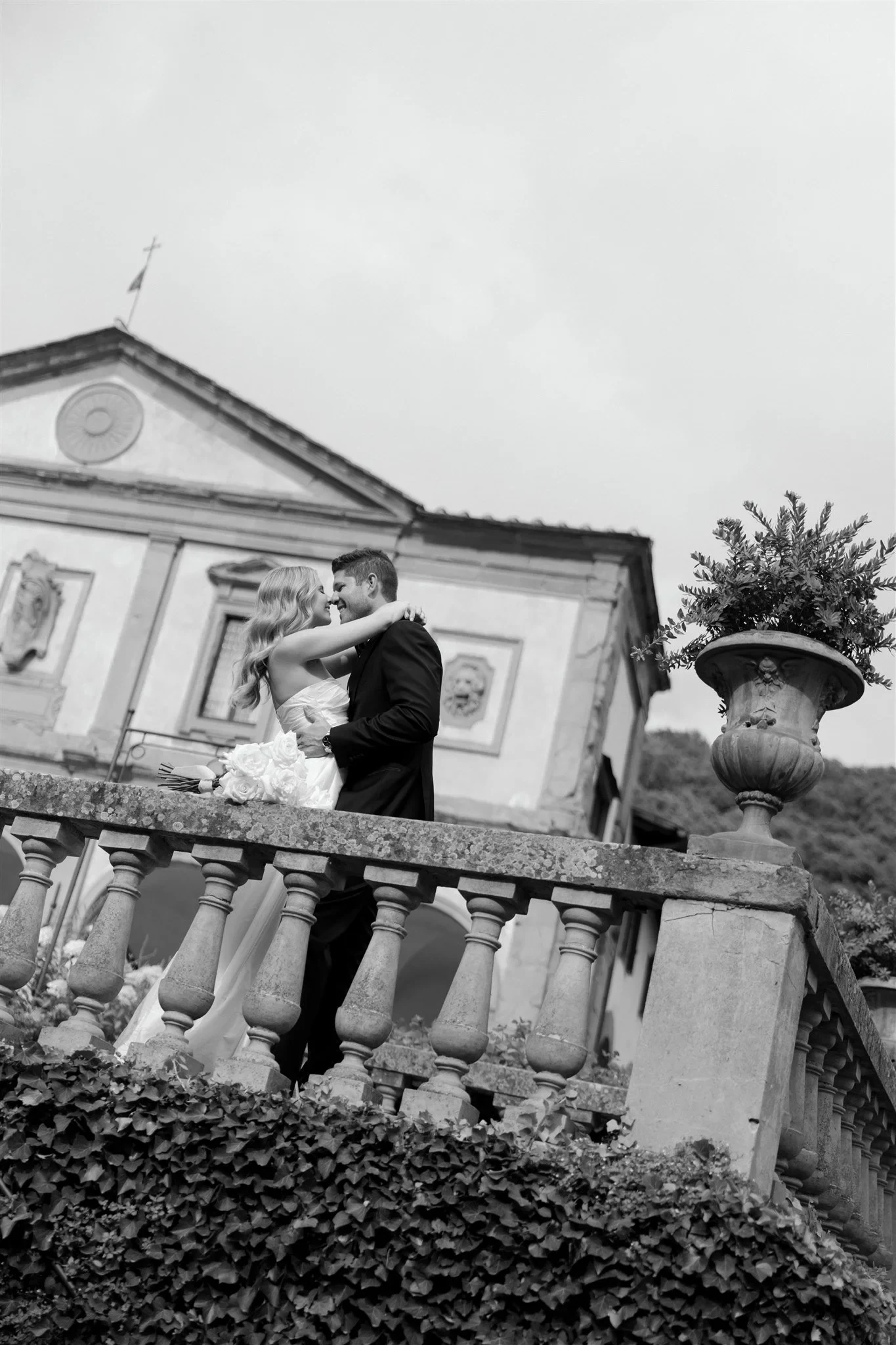 Black-and-white photograph of Holly and Matt embracing above the garden, with the villa façade behind them, at Belmond Villa San Michele in Fiesole, overlooking Florence, Tuscany, Italy, for an Elopement Collective elopement. Photo by Khara from House of Lucie.