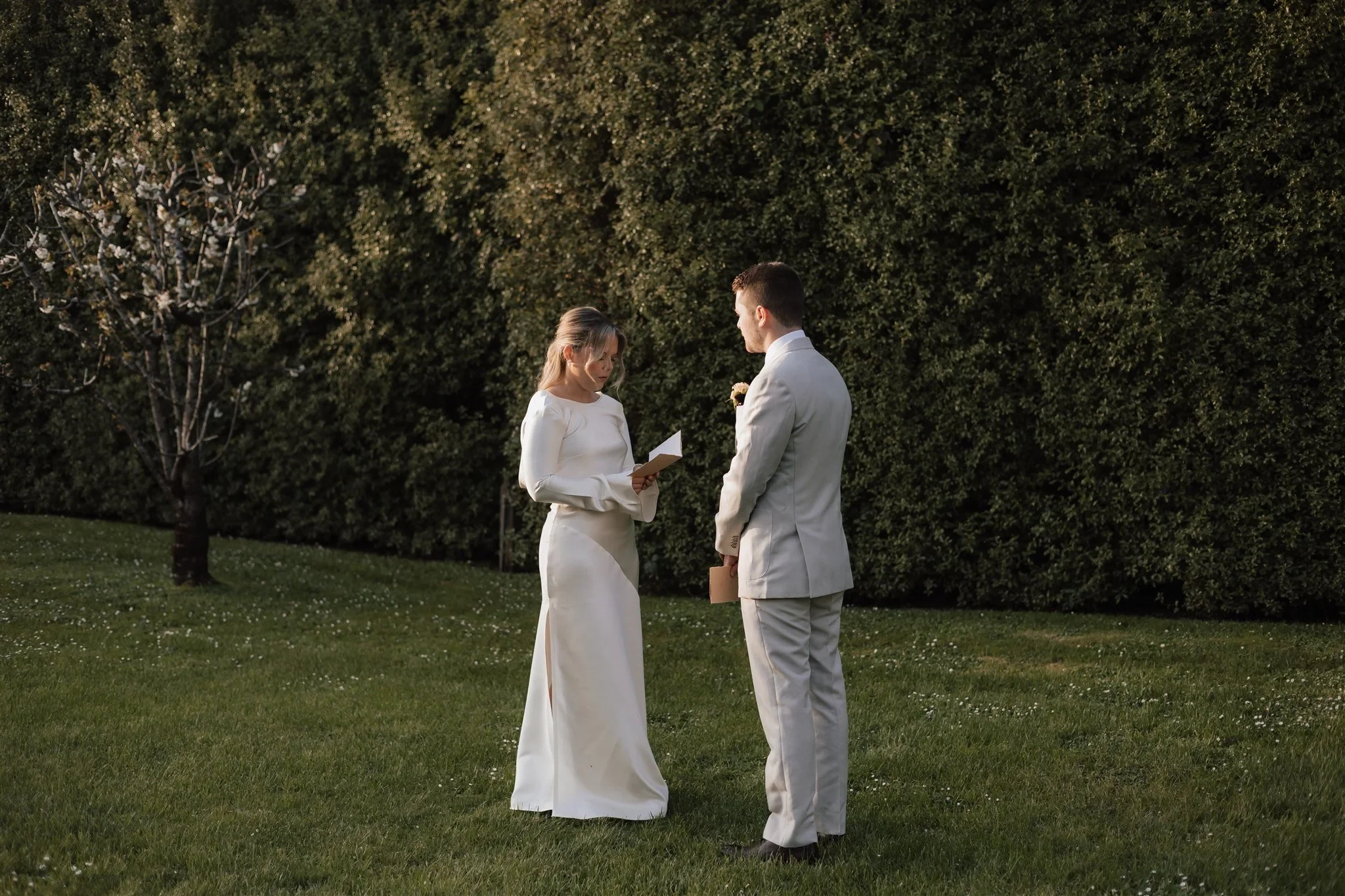 Maddy reading from her vow booklet as Cameron listens on the lawn, at The Mayor’s Residence in Daylesford, Victoria, for an Elopement Collective elopement. Photo by Bulb Creative.