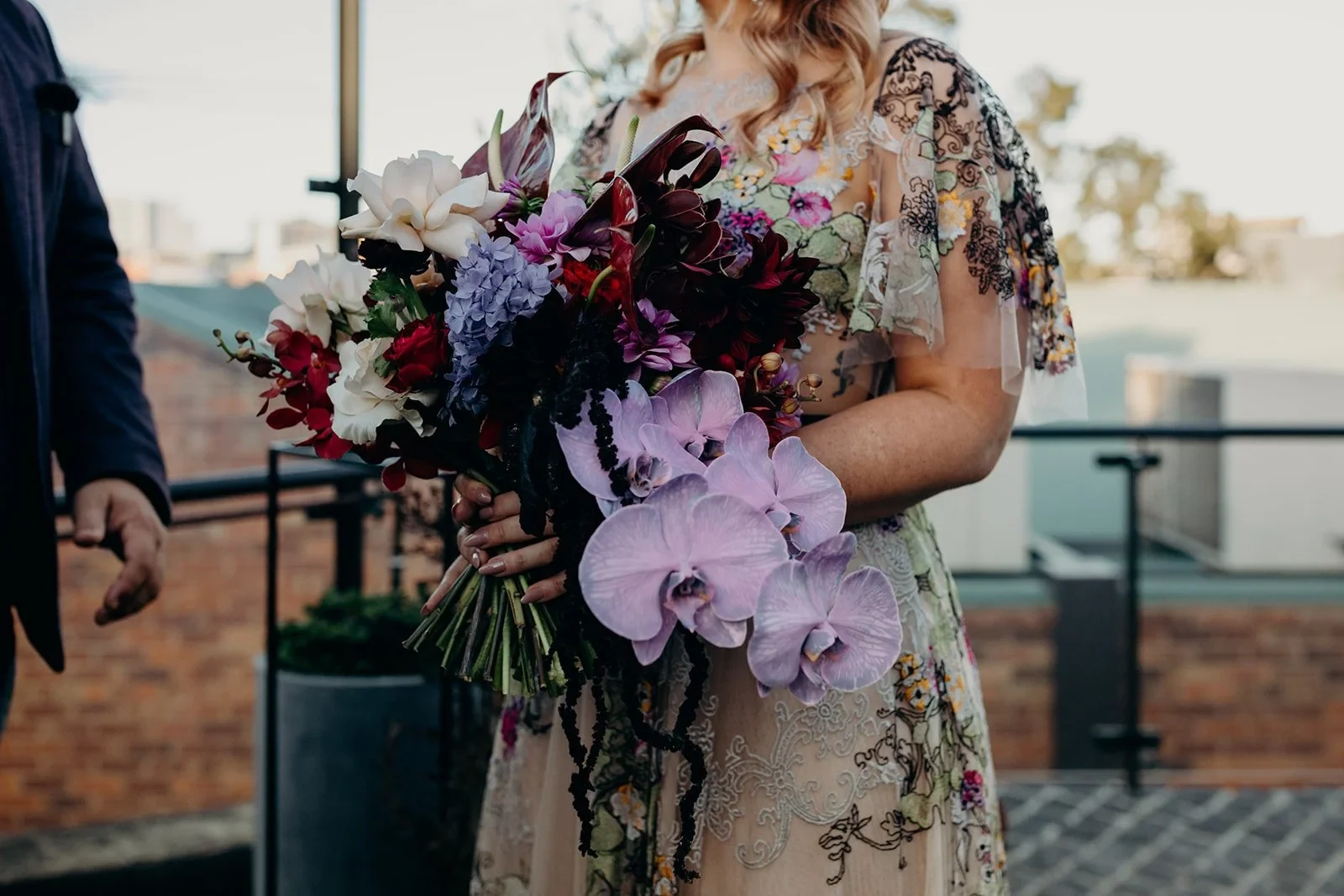 Close-up of Victoria holding a cascading bouquet of purple orchids and burgundy blooms by Mrs Gibbons Flowers, at Agnes Restaurant in Fortitude Valley, Brisbane, for an Elopement Collective elopement. Photo by Tessa Shannon.