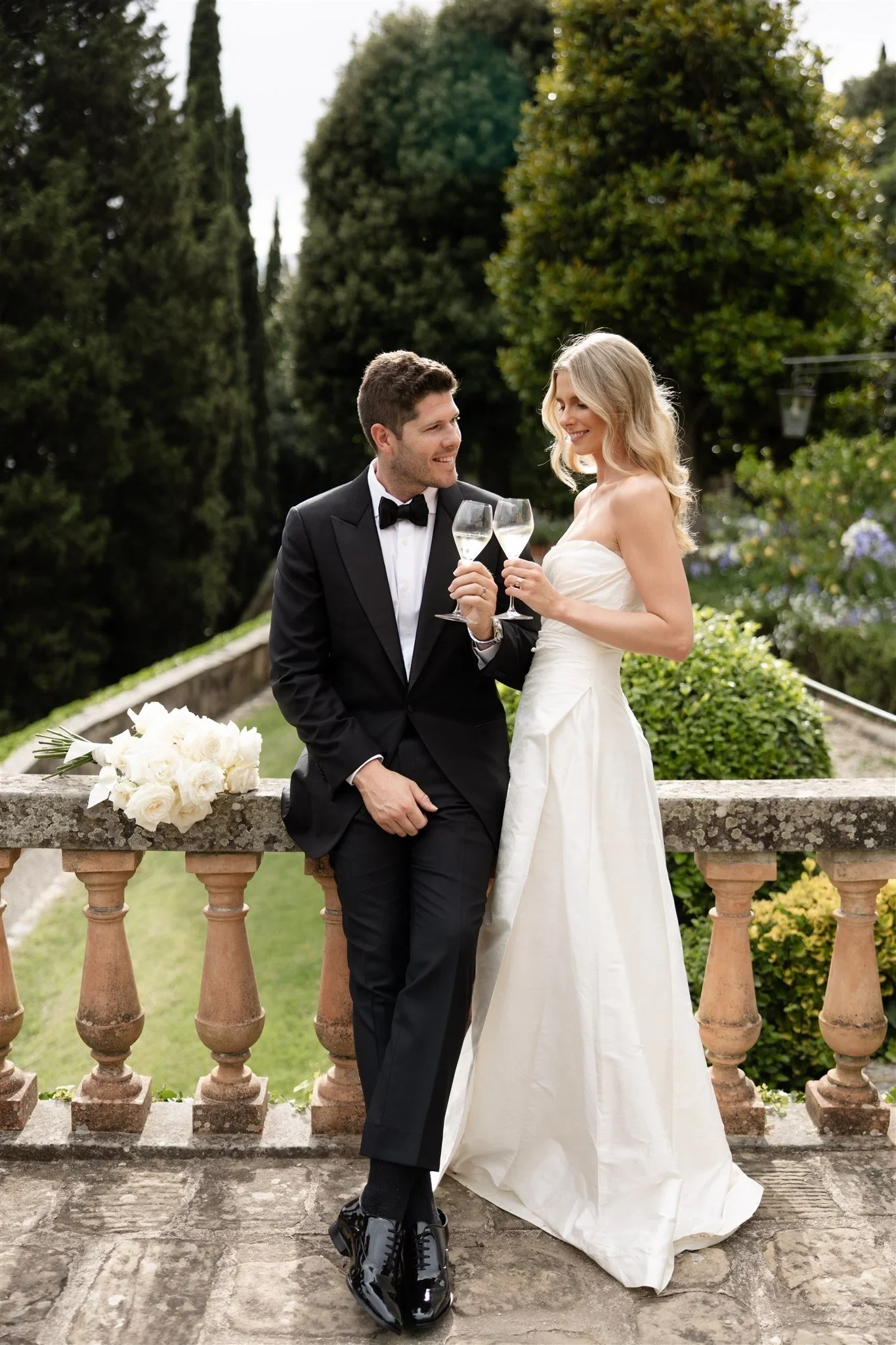 Holly and Matt sharing drinks beside her white bouquet by Le Francesche on the terrace, at Belmond Villa San Michele in Fiesole, overlooking Florence, Tuscany, Italy, for an Elopement Collective elopement. Photo by Khara from House of Lucie.