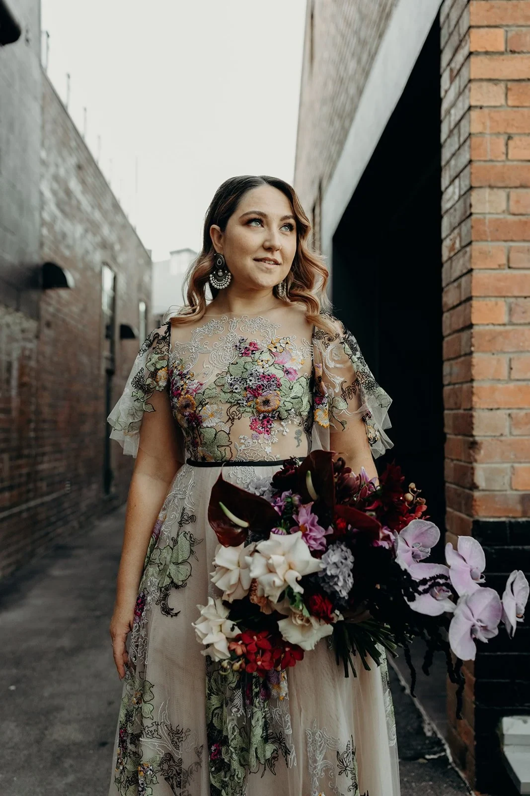 Victoria standing in a narrow laneway with her colourful bouquet by Mrs Gibbons Flowers, in Fortitude Valley, Brisbane, for an Elopement Collective elopement. Photo by Tessa Shannon.