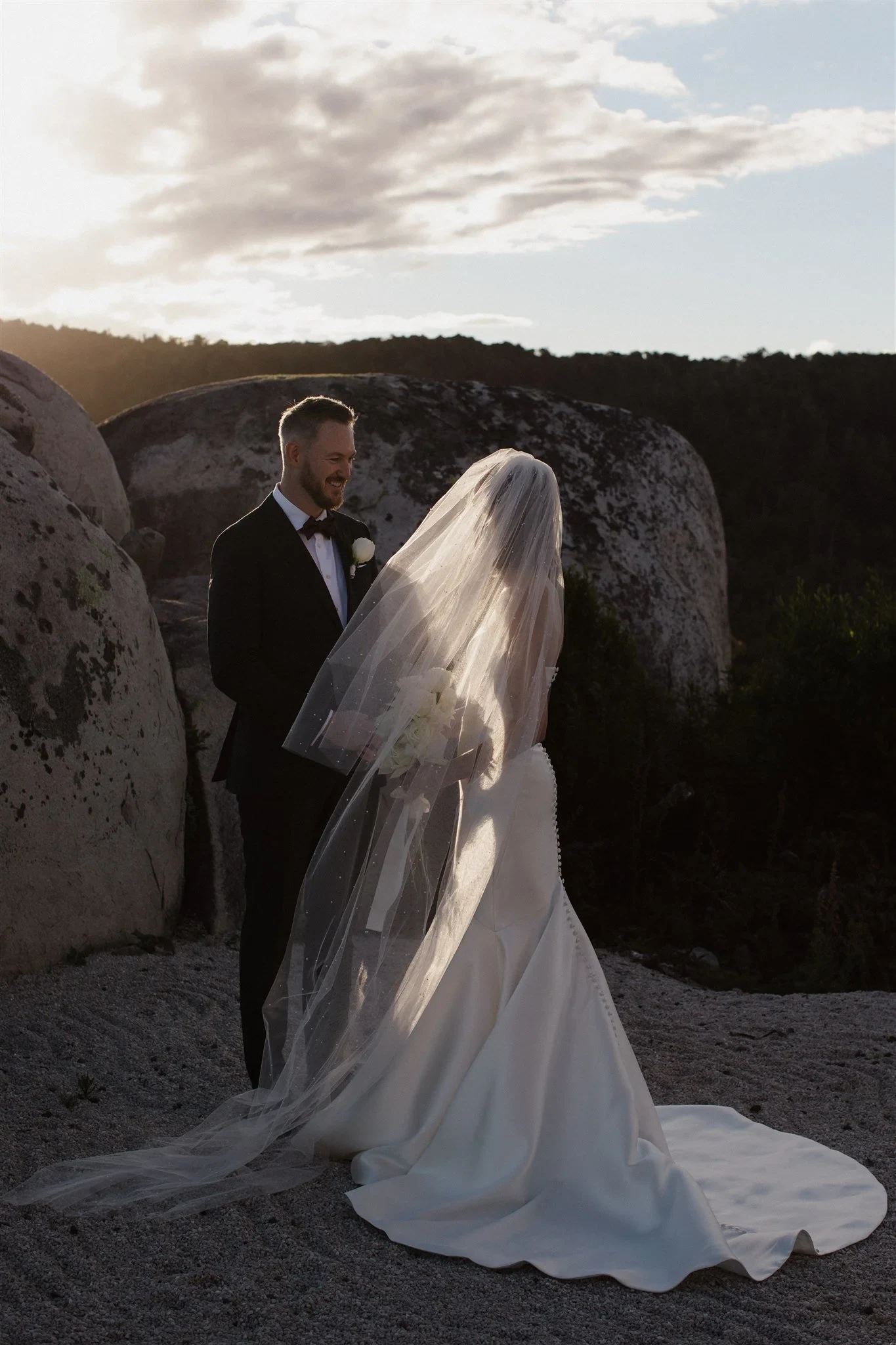 A couple facing one another among granite boulders in the evening light, during a Tasmanian elopement created by The Elopement Collective.