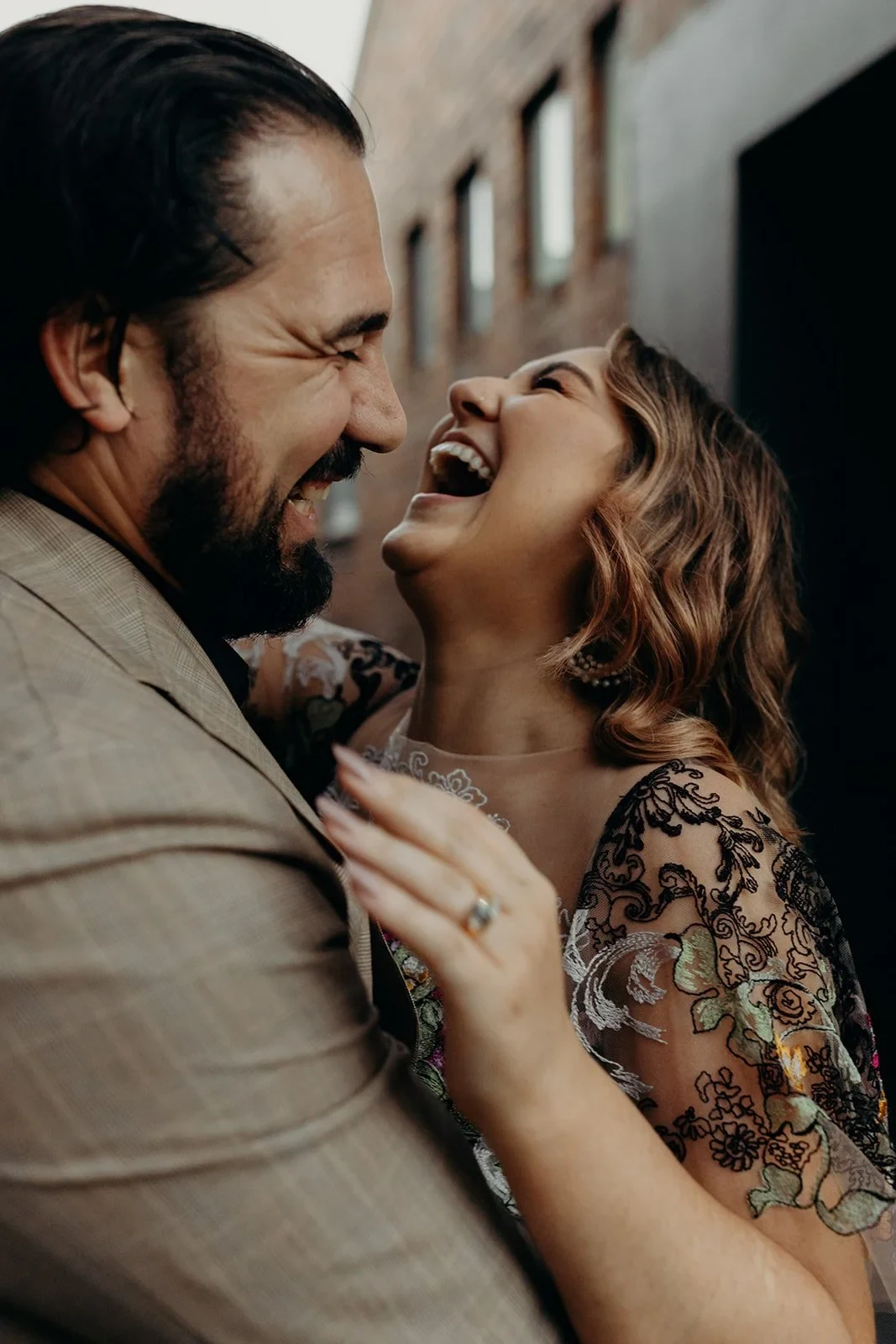 Close-up of Victoria laughing in Daniel’s arms against a brick wall, in Fortitude Valley, Brisbane, for an Elopement Collective elopement. Photo by Tessa Shannon.