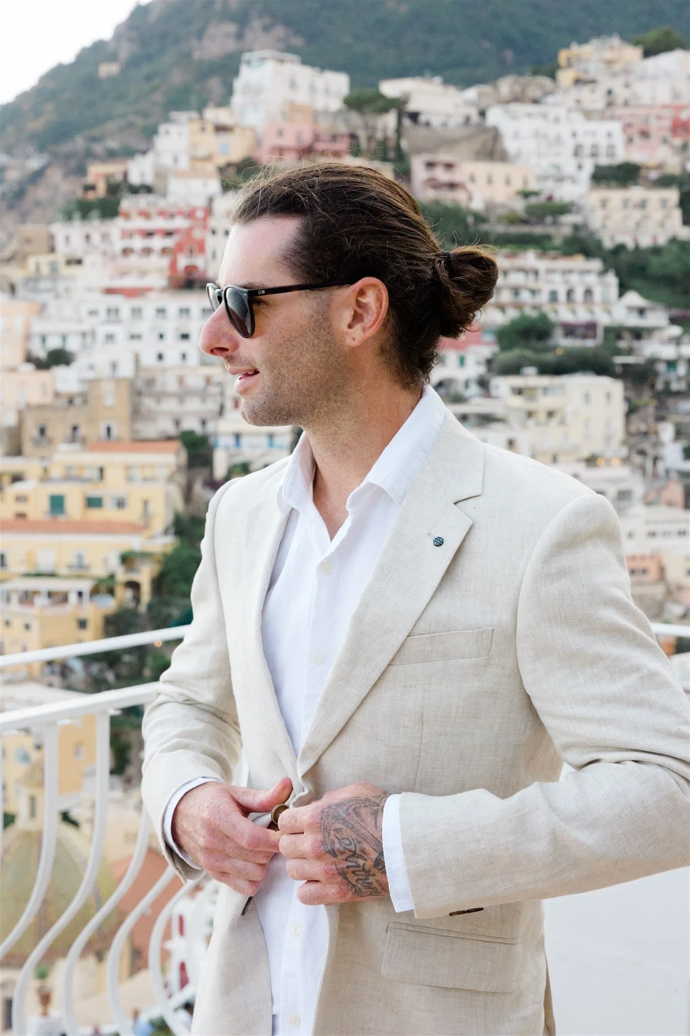Groom Josh adjusting his light linen jacket on the terrace above the hillside town, at Alcione Residence in Positano, Amalfi Coast, Italy, for an Elopement Collective elopement. Photo by James from House of Love.