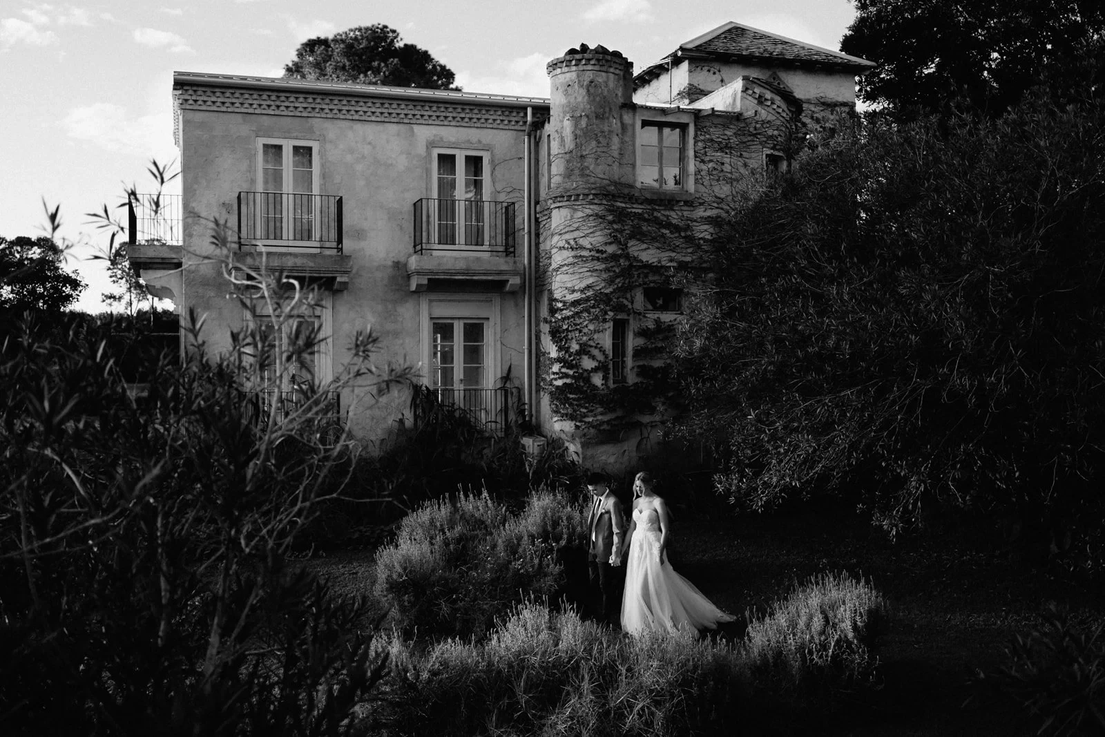 A couple holding hands in a garden below a vine-covered villa, during a Byron Bay elopement created by The Elopement Collective.