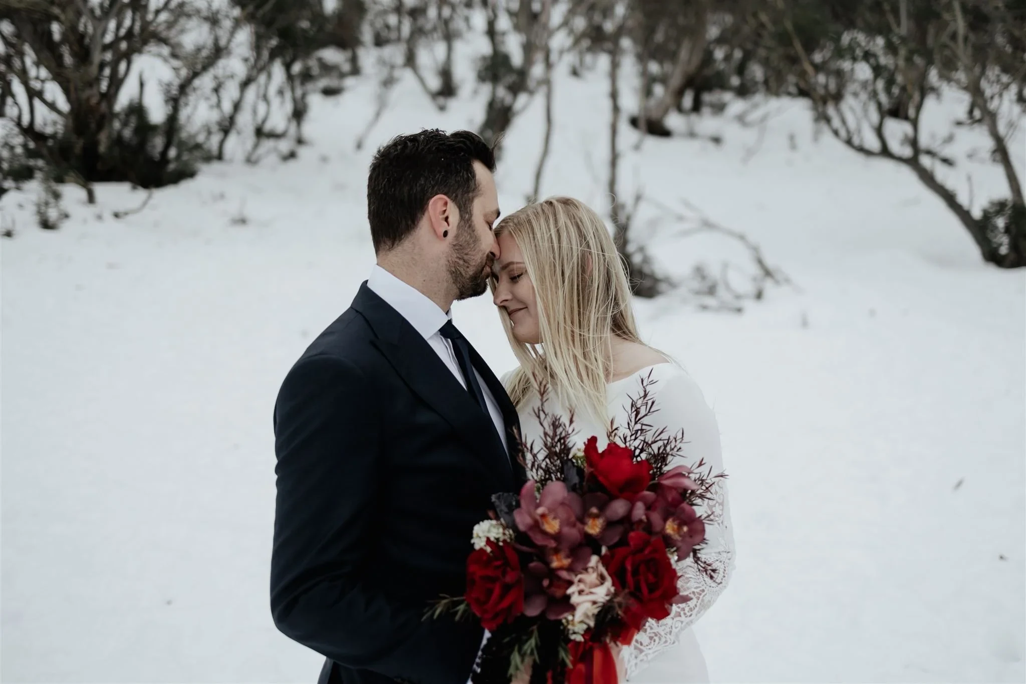 Couple embracing in the snow with a red and burgundy wedding bouquet