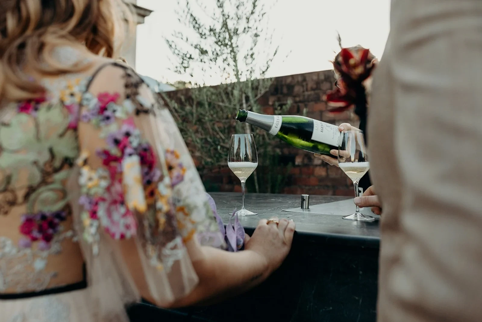 Sparkling wine being poured into glasses beside Victoria and Daniel on the rooftop terrace, at Agnes Restaurant in Fortitude Valley, Brisbane, for an Elopement Collective elopement. Photo by Tessa Shannon.