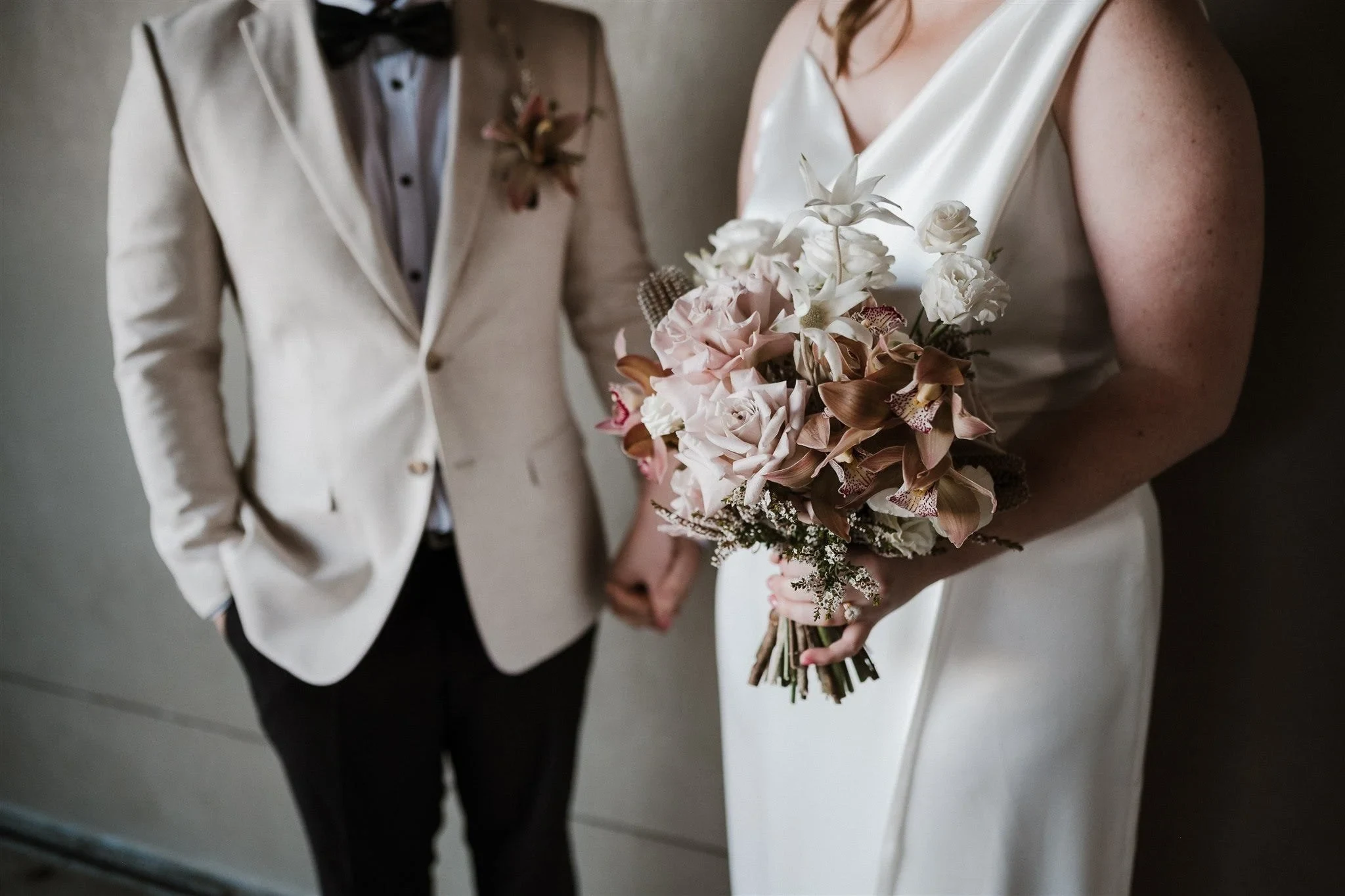 Close view of Alyce’s pink and white bouquet by The Lillipillian beside Andrew’s cream jacket and floral pocket arrangement, in The Rocks, Sydney, New South Wales, for an Elopement Collective elopement. Photo by Jason Corroto.