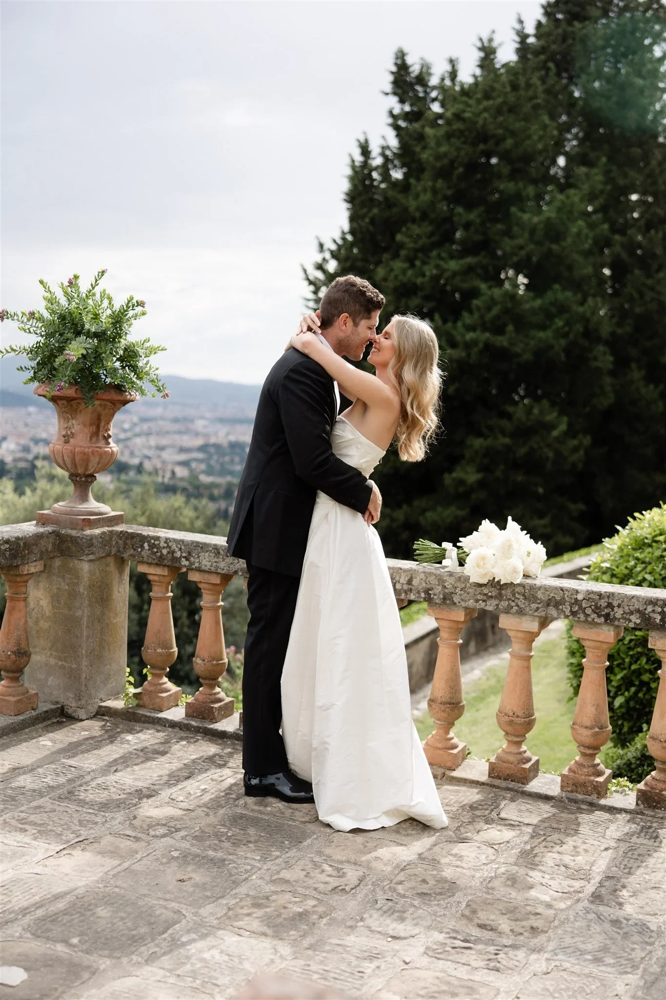 Holly and Matt kissing beside the stone balustrade and potted plants, at Belmond Villa San Michele in Fiesole, overlooking Florence, Tuscany, Italy, for an Elopement Collective elopement. Photo by Khara from House of Lucie.
