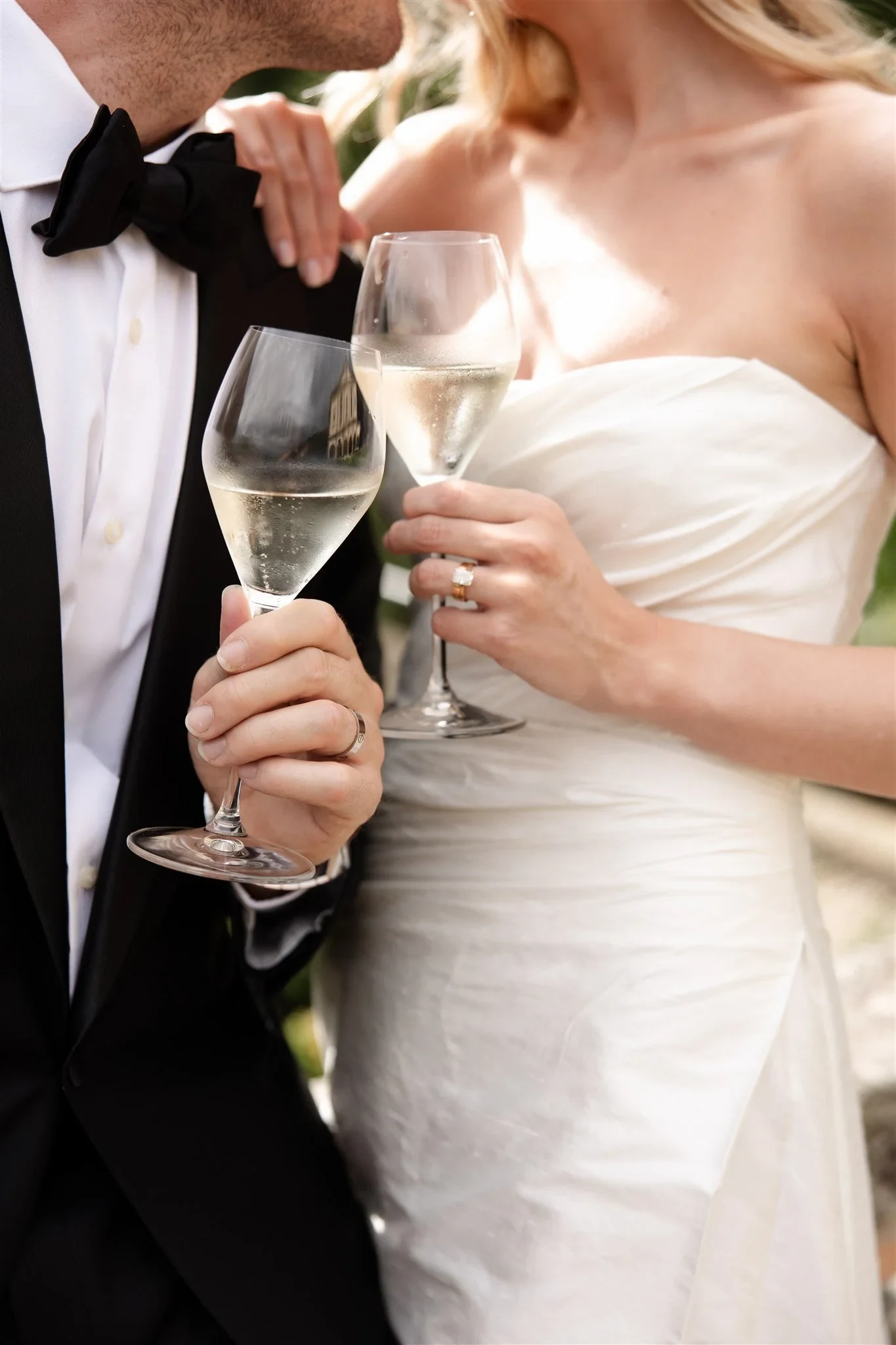 Close view of Holly and Matt holding glasses of white wine beside her draped dress and his black bow tie, at Belmond Villa San Michele in Fiesole, overlooking Florence, Tuscany, Italy, for an Elopement Collective elopement. Photo by Khara from House of Lucie.