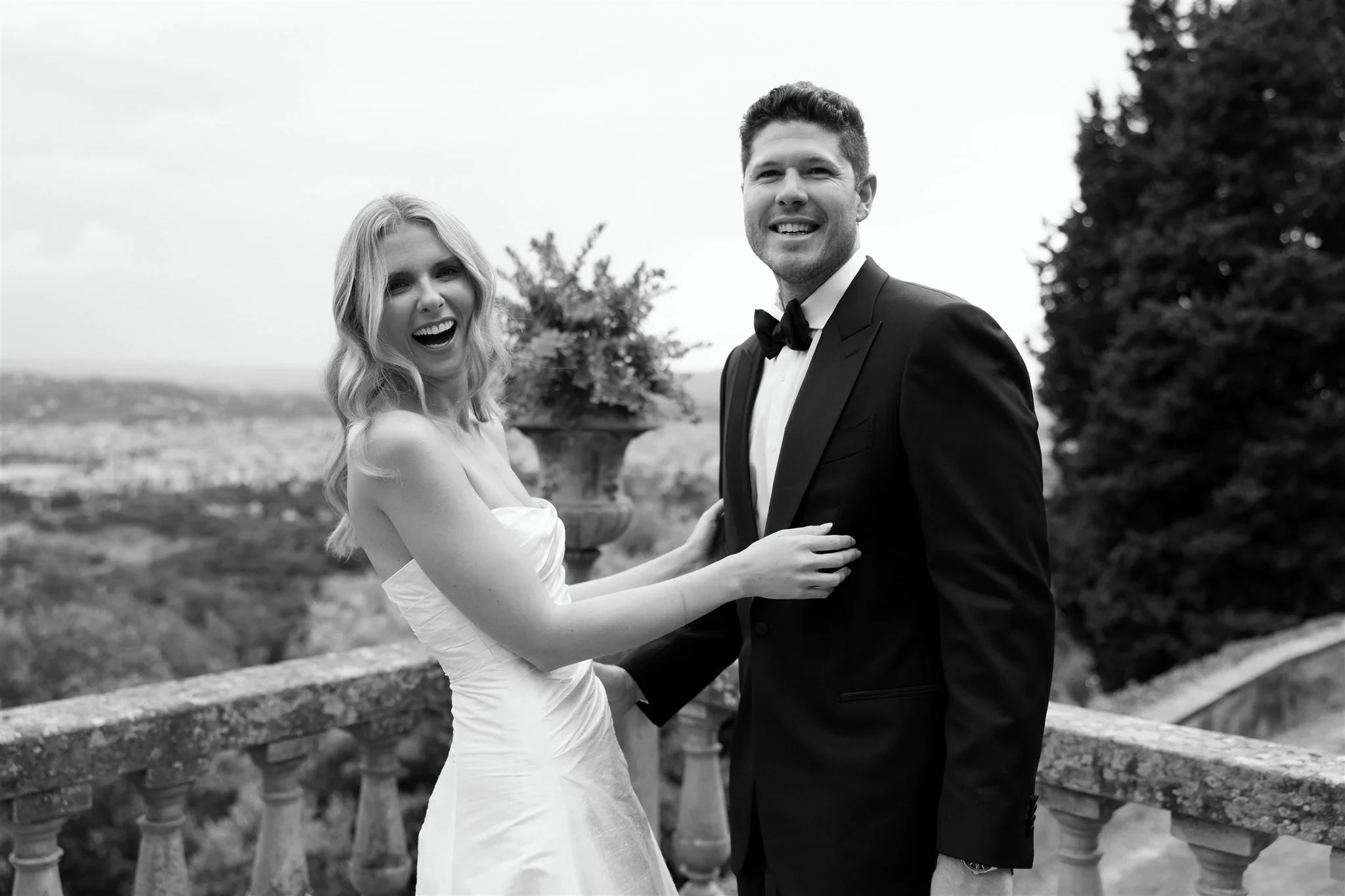 Black-and-white photograph of Holly and Matt laughing together above the Florence skyline, at Belmond Villa San Michele in Fiesole, overlooking Florence, Tuscany, Italy, for an Elopement Collective elopement. Photo by Khara from House of Lucie.