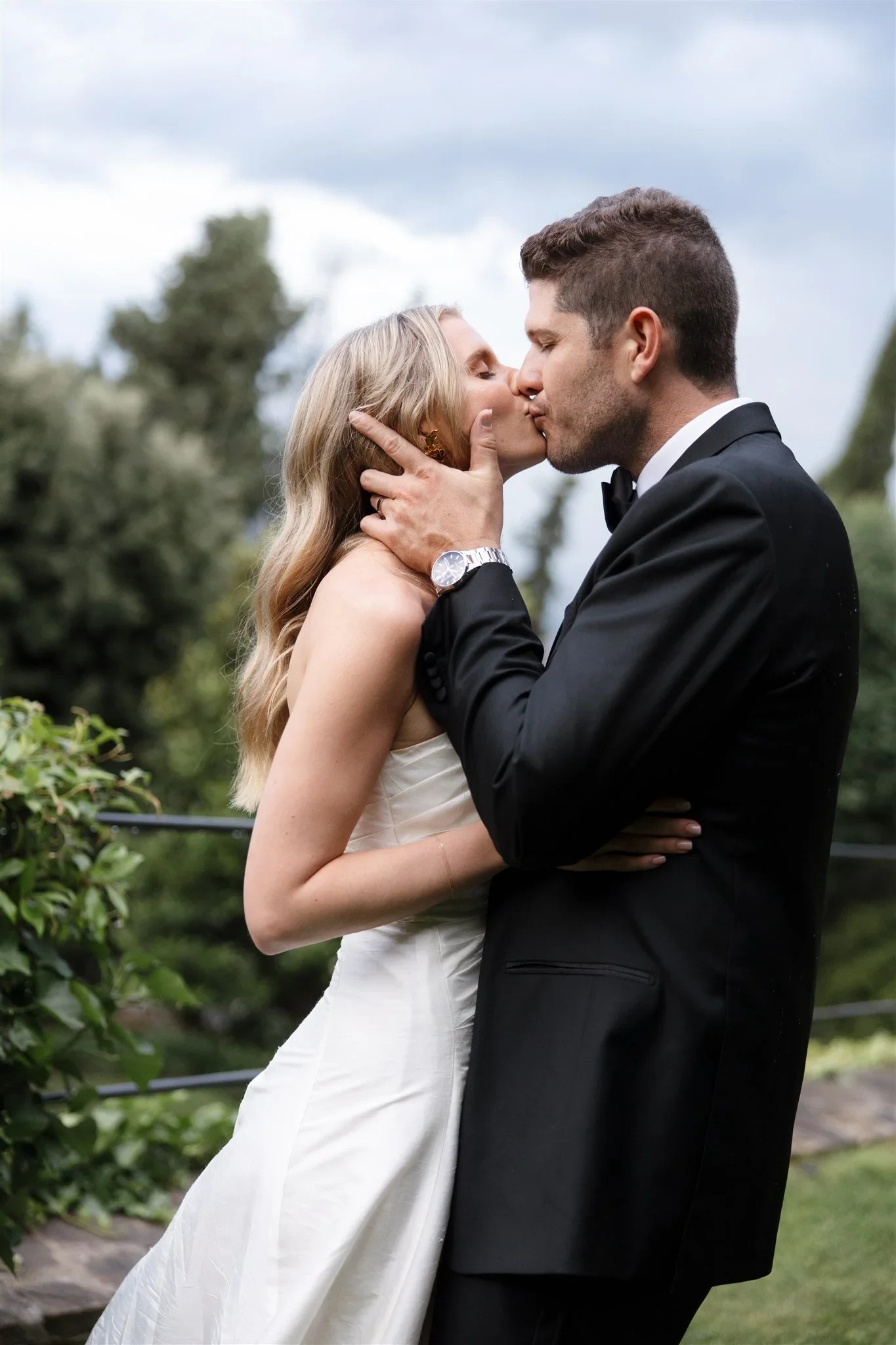 Matt holding Holly’s face as they kiss beneath leafy trees, at Belmond Villa San Michele in Fiesole, overlooking Florence, Tuscany, Italy, for an Elopement Collective elopement. Photo by Khara from House of Lucie.