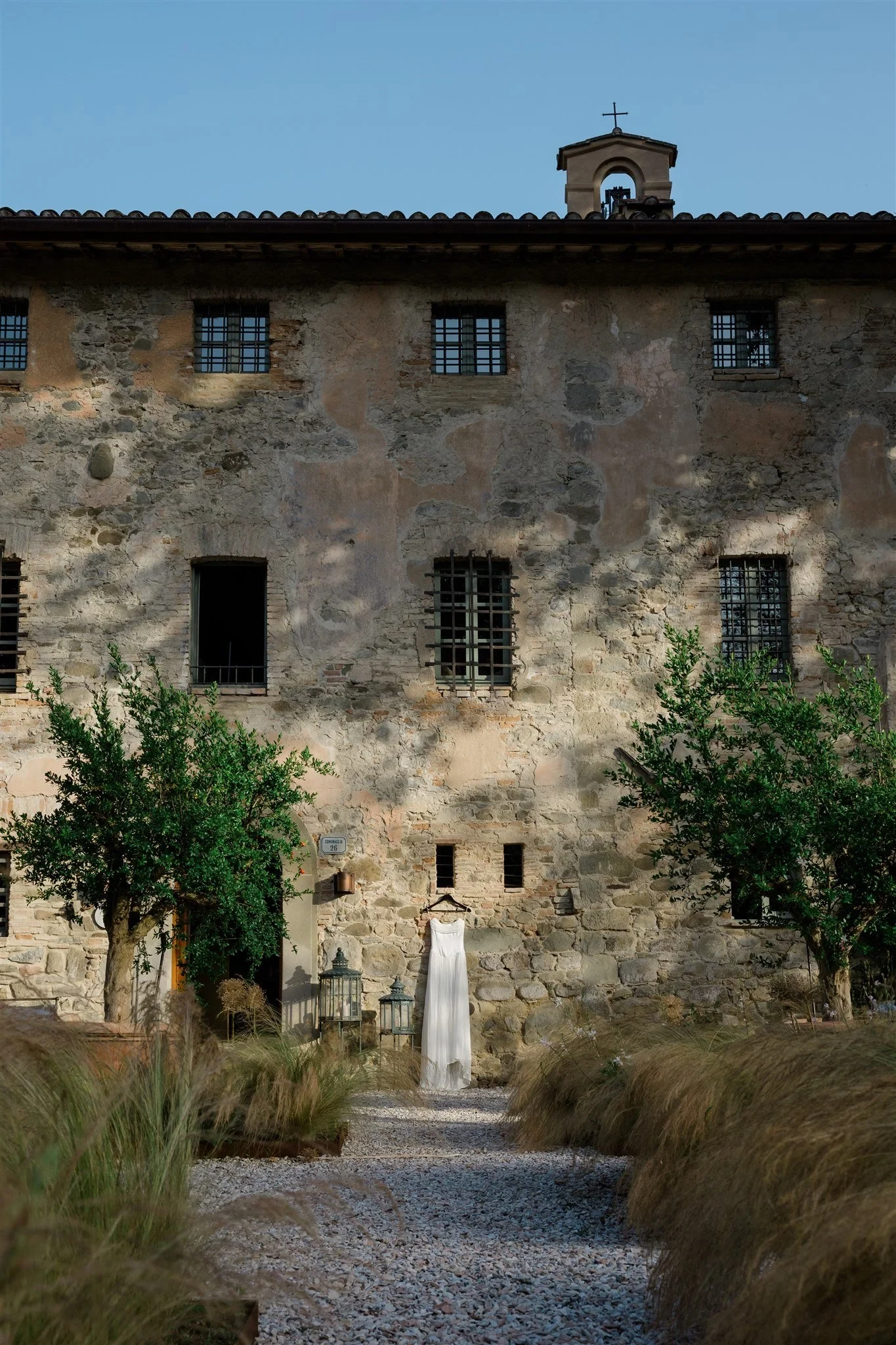 A stone country building at the end of a gravel path lined with ornamental grasses, in Umbria, Italy, for an Elopement Collective elopement. Photo by James from House of Love.
