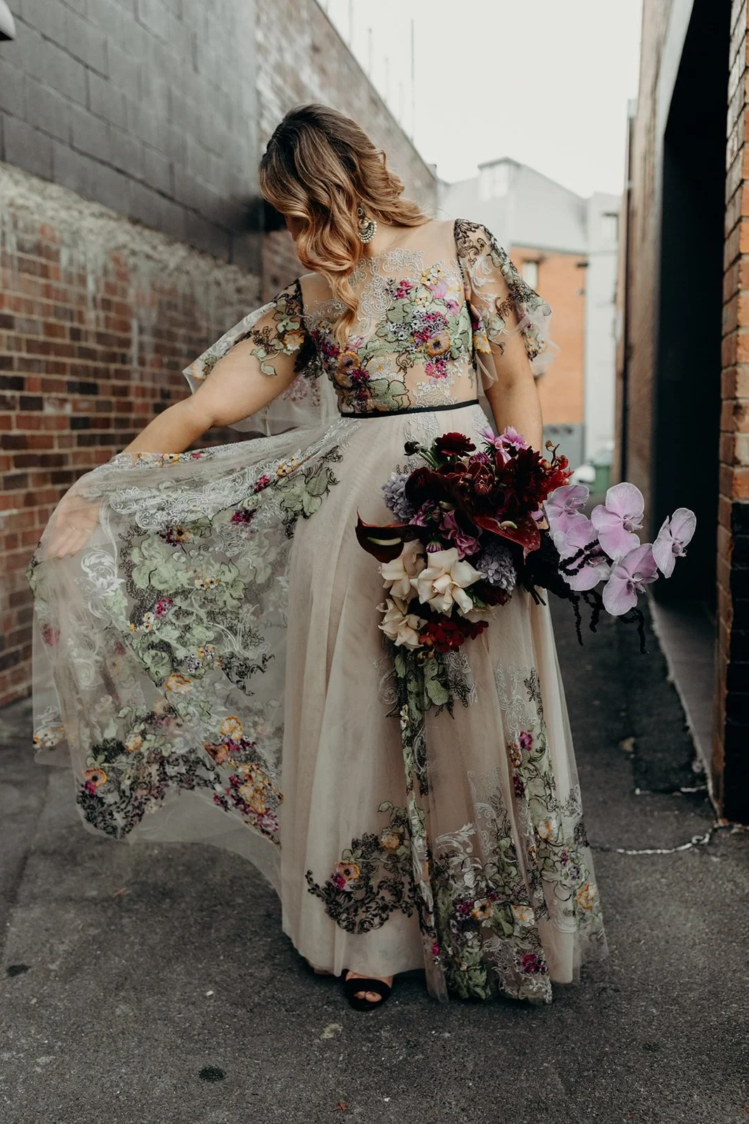 Victoria looking down at her flowing floral dress while holding her bouquet by Mrs Gibbons Flowers, in Fortitude Valley, Brisbane, for an Elopement Collective elopement. Photo by Tessa Shannon.