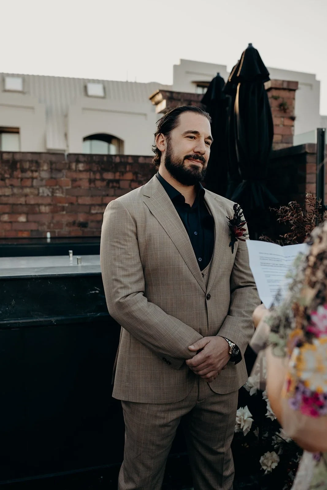 Daniel listening to Victoria’s vows with his hands clasped in front of his beige suit, at Agnes Restaurant in Fortitude Valley, Brisbane, for an Elopement Collective elopement. Photo by Tessa Shannon.