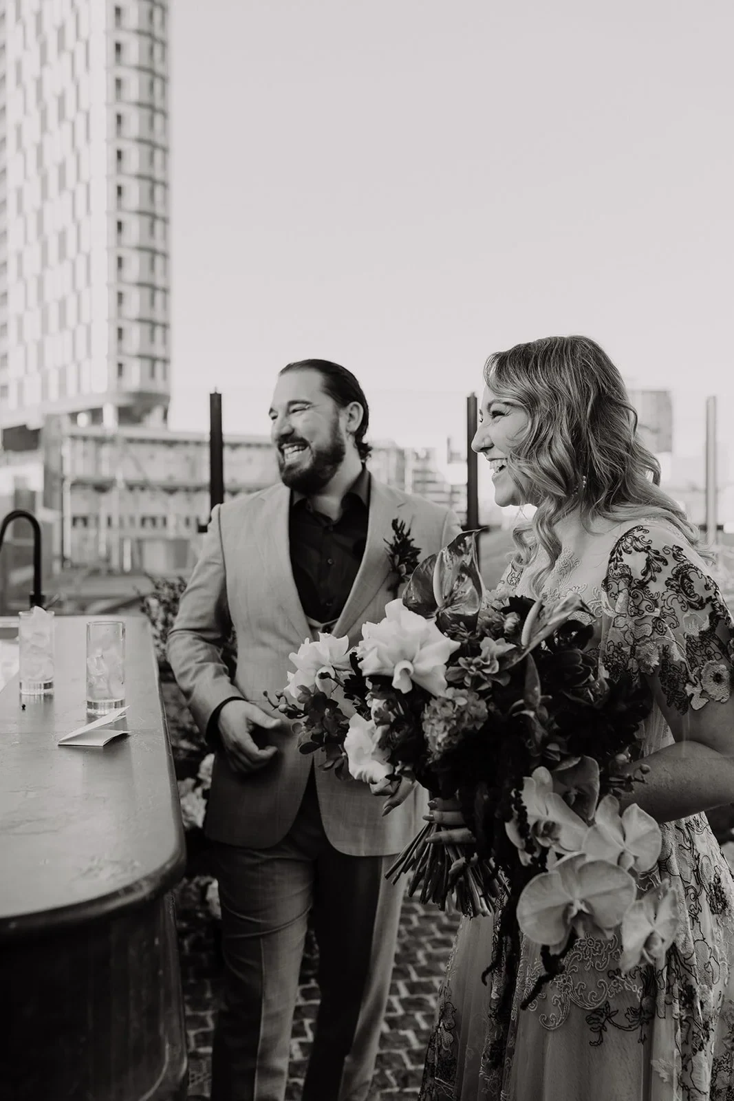 Black-and-white portrait of Victoria and Daniel on the rooftop terrace with her bouquet by Mrs Gibbons Flowers, at Agnes Restaurant in Fortitude Valley, Brisbane, for an Elopement Collective elopement. Photo by Tessa Shannon.