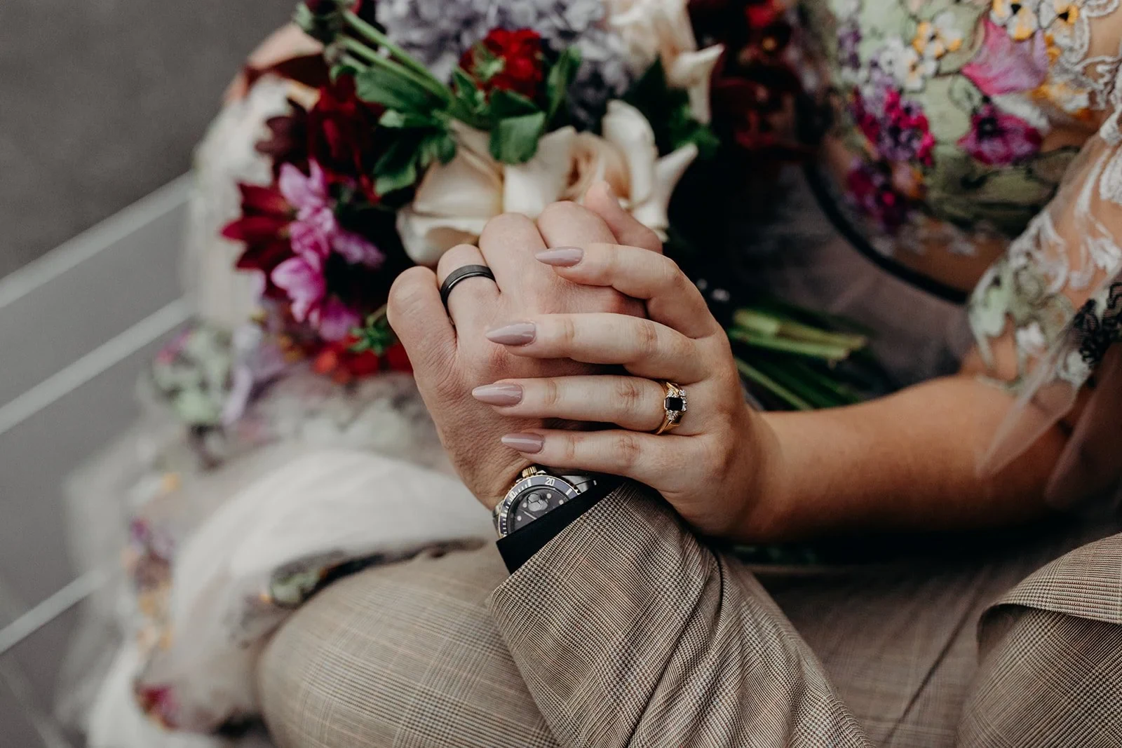 Close-up of Victoria and Daniel’s clasped hands and wedding rings, with her bouquet by Mrs Gibbons Flowers beside them, in Fortitude Valley, Brisbane, for an Elopement Collective elopement. Photo by Tessa Shannon.